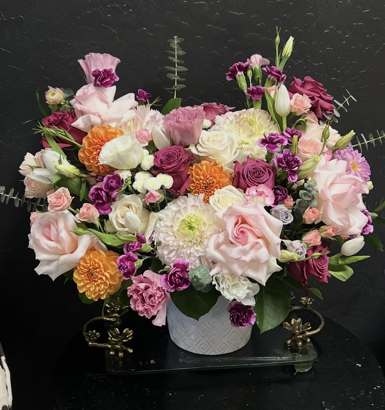 Garden Romance Bouquet  - Lush blush and white garden roses take center stage in this Garden Romance bouquet, a full, low-to-medium flower arrangement perfect for a birthday, a heartfelt "I'm sorry," or a quiet just-because surprise. The mix leans romantic without being fussy-soft pinks and purples meet pops of orange to create a cheerful, celebratory palette that reads as both intimate and festive for the person you're thinking of.  Built like a garden-style centerpiece, the bouquet combines garden roses, classic roses, carnations, chrysanthemums, tulip buds, lisianthus, and assorted small accent blooms for layered texture and movement. Arranged tightly for a generous look, it comes in a white textured ceramic vase that gives the design a polished everyday presentation and makes it ready to display on a table, desk, or bedside. Dimensions are low-to-medium height to suit tabletops and mantels.  Whether you're marking an anniversary, saying "I miss you," or simply wanting someone to feel genuinely seen, this arrangement delivers warmth and romance. To keep blooms looking their best, refresh water every two days and trim stems slightly when rewatering; the ceramic vase is perfect for gifting as-is and makes the bouquet an easy, thoughtful statement of care.