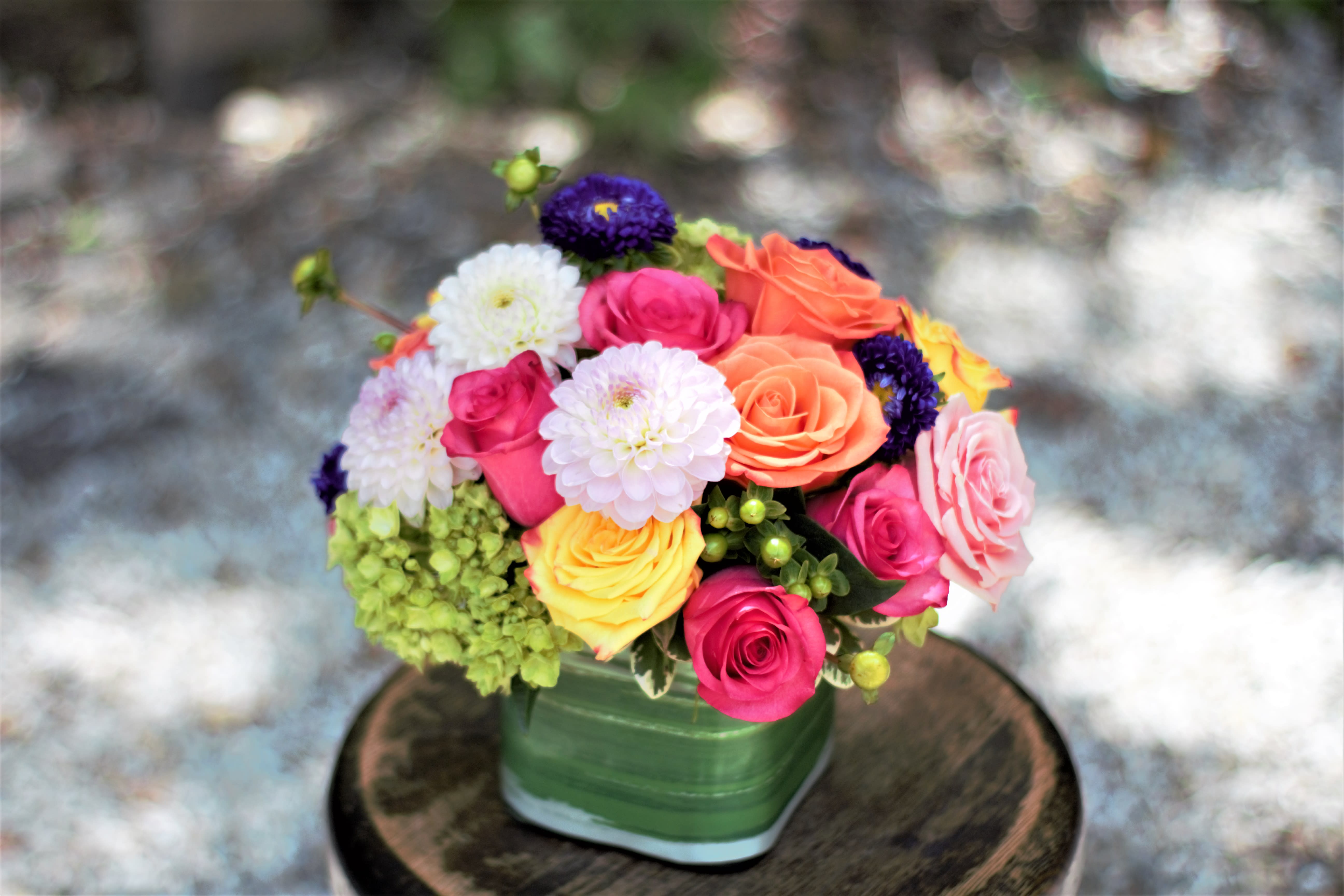 Colorful bouquet of roses and pom-pom flowers in a green vase
