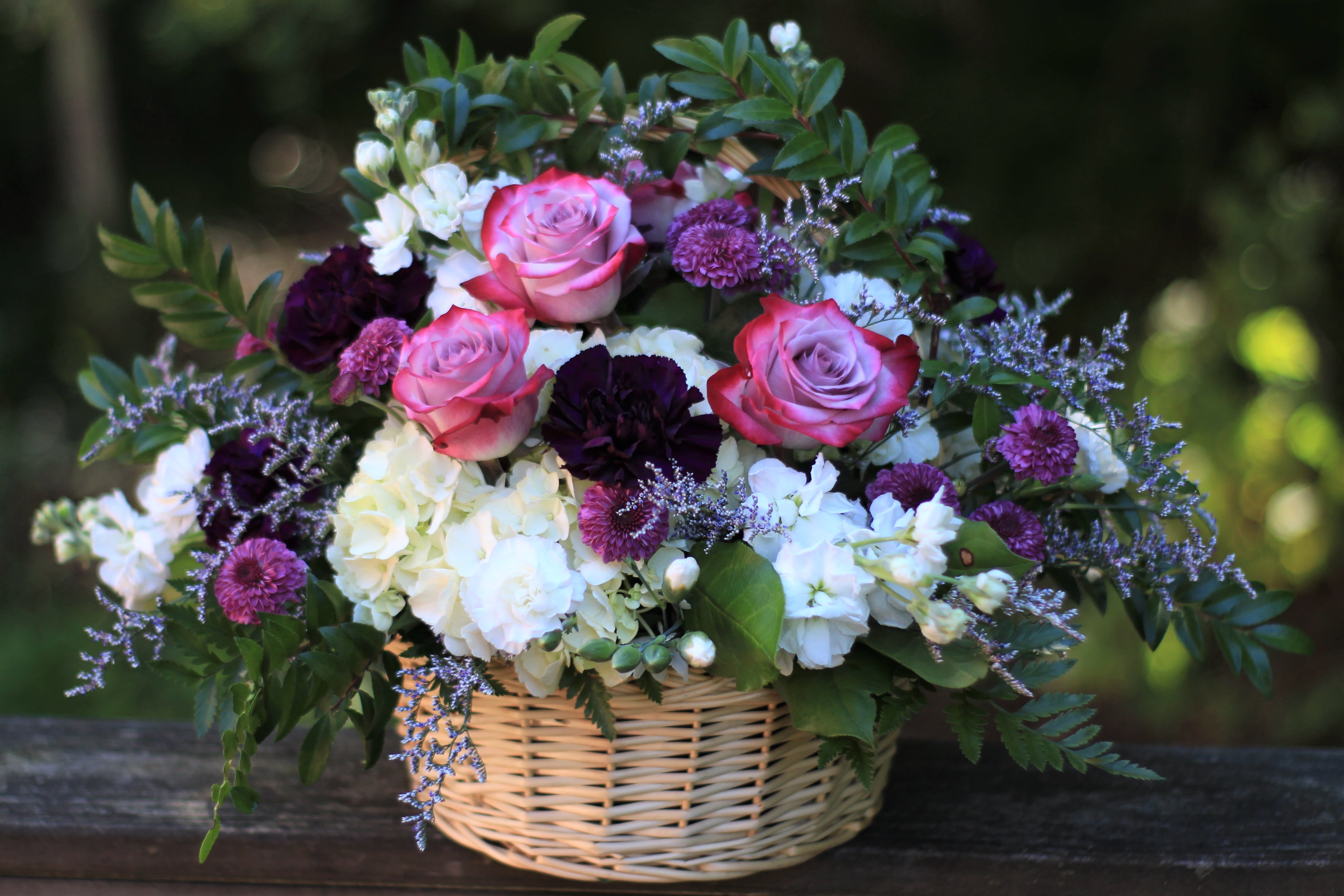 Basket arrangement of pink roses, white hydrangeas, and purple flowers