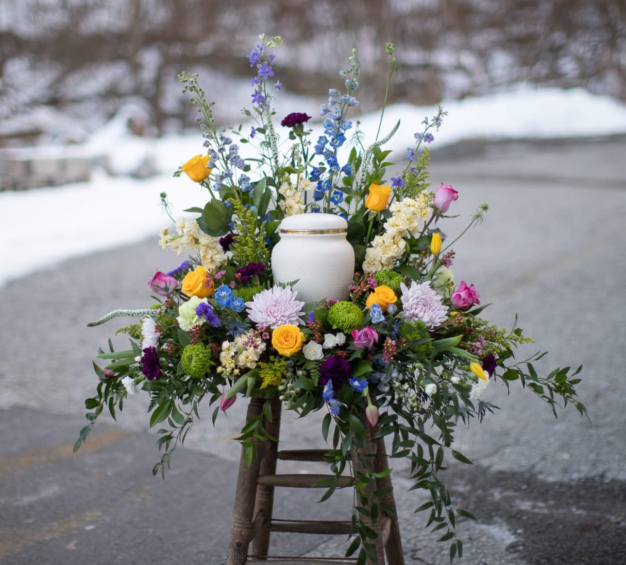 Colorful floral arrangement around a white urn on a stool