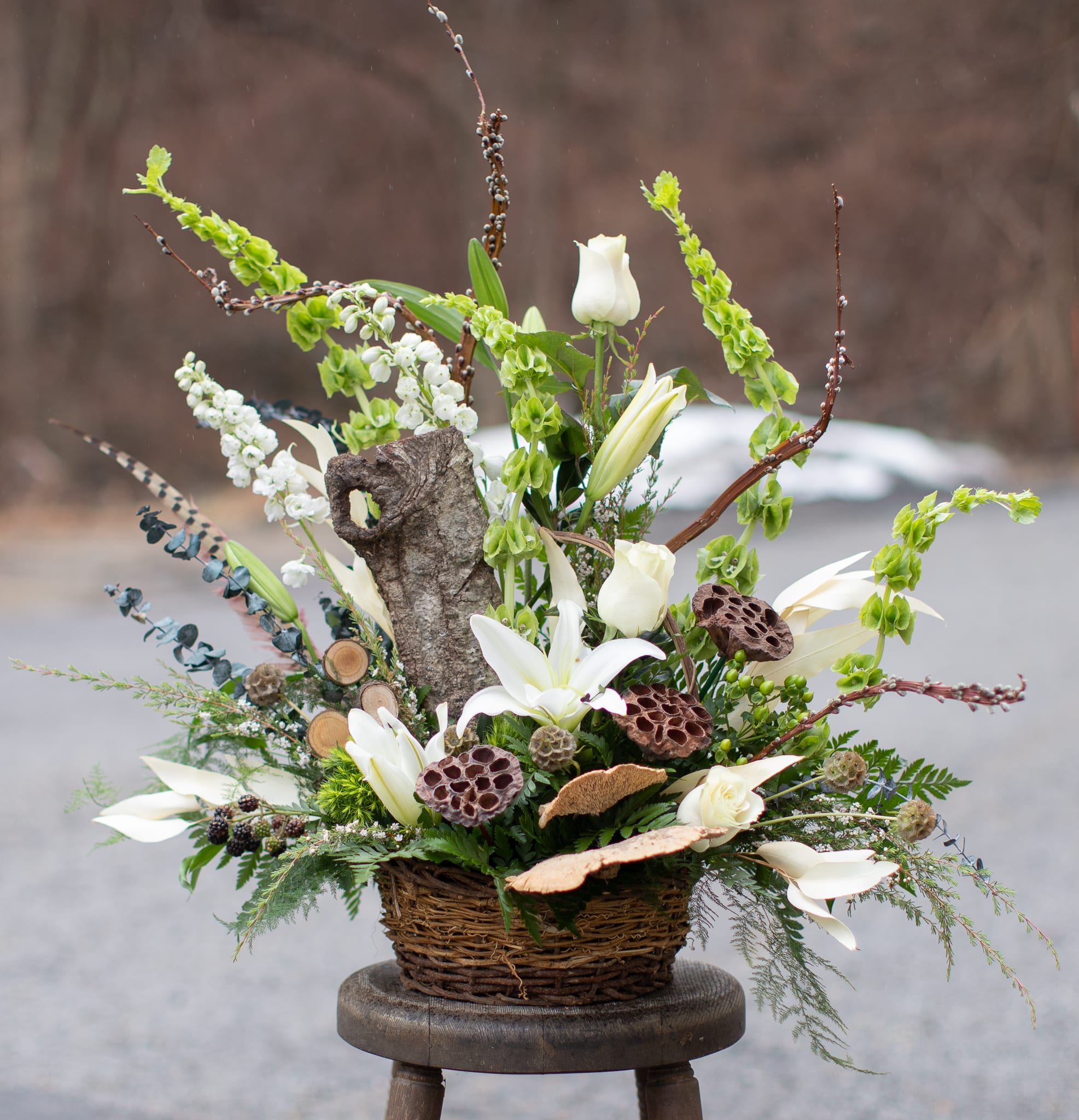 White lilies and roses in a wicker basket with branches and seed pods