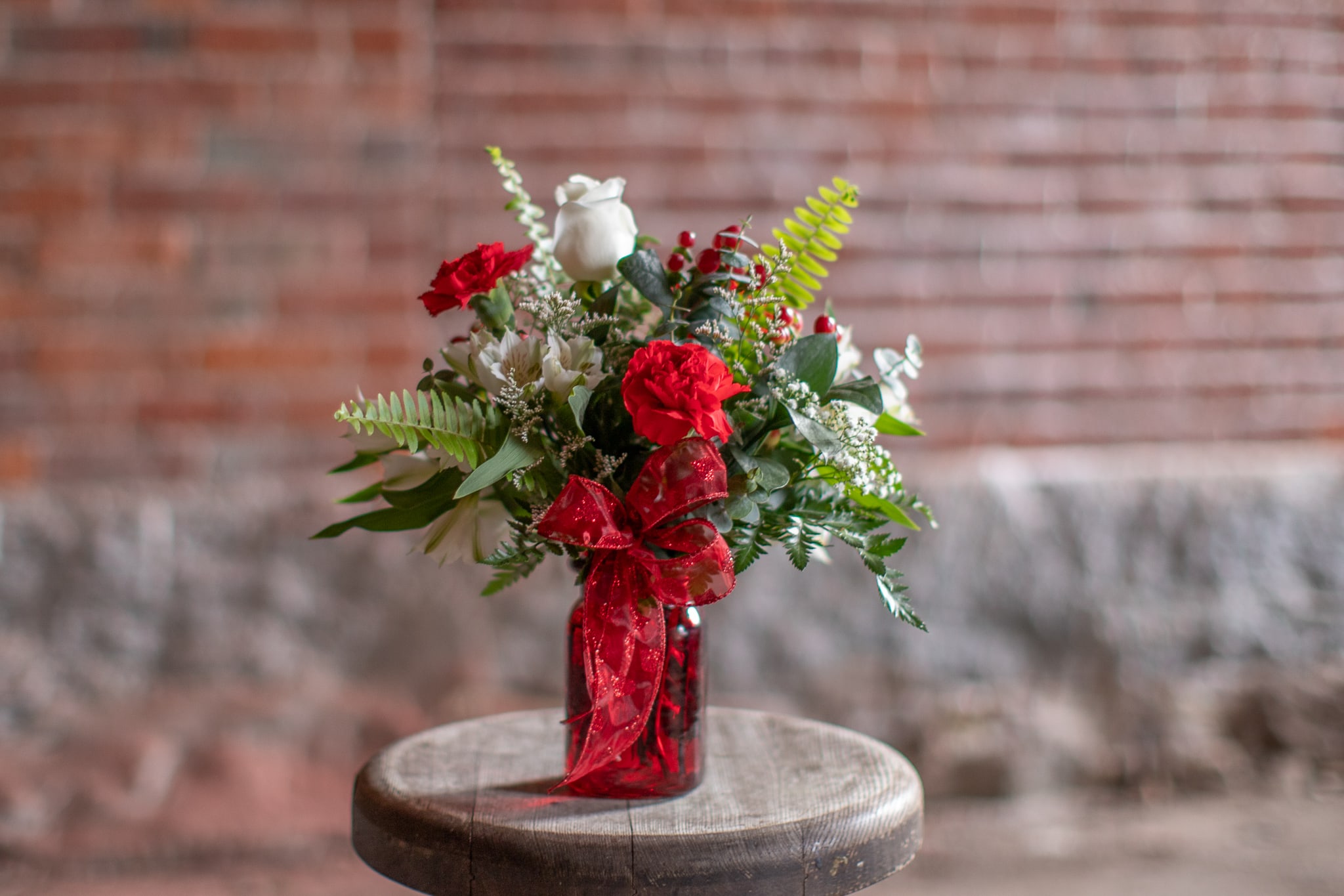 Red and white floral arrangement in a red glass vase with a ribbon