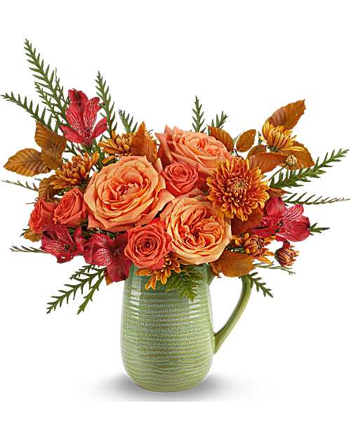Orange roses and red flowers arranged in a green ceramic pitcher