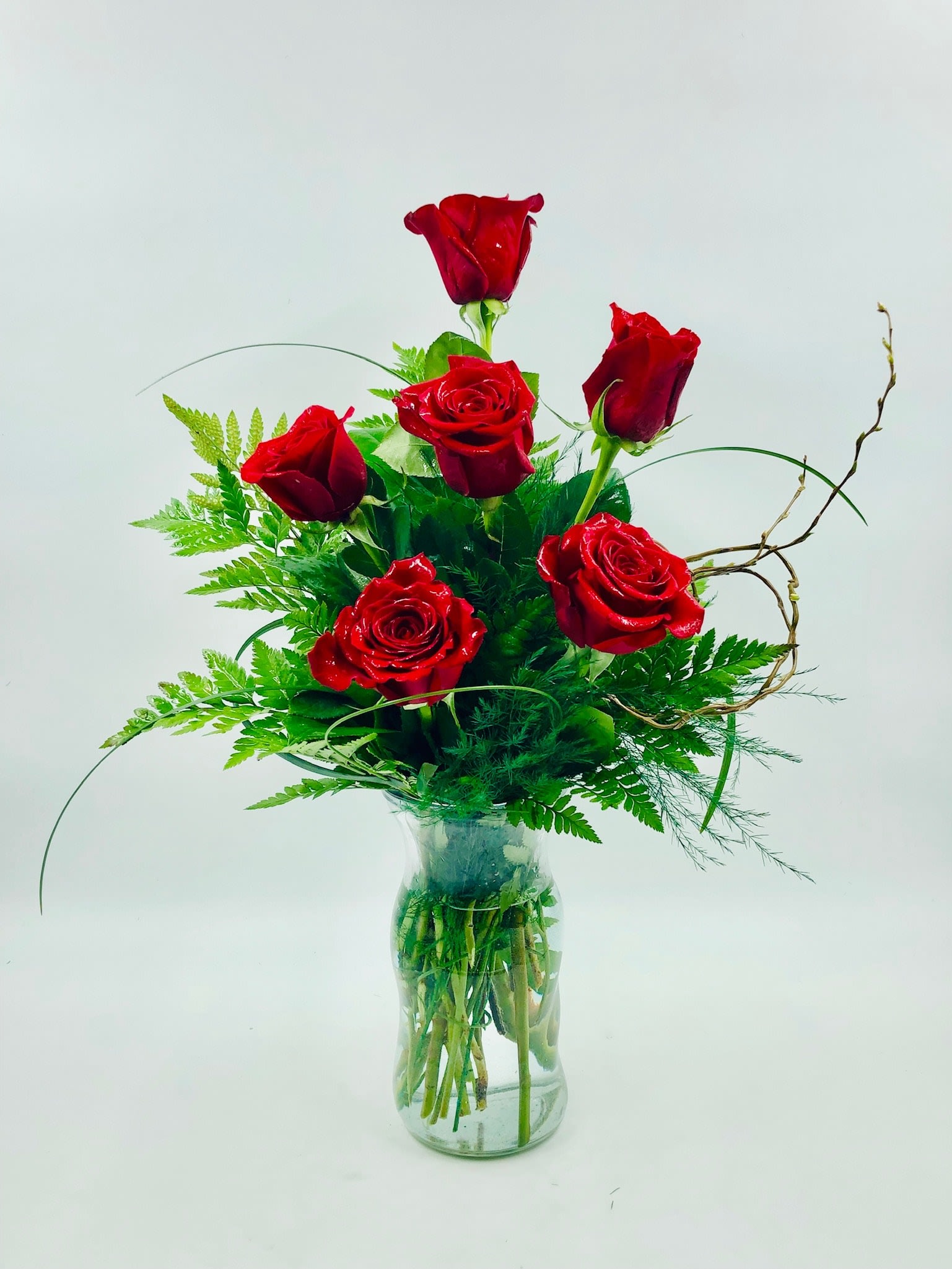 Red roses arranged in a clear glass vase with green foliage