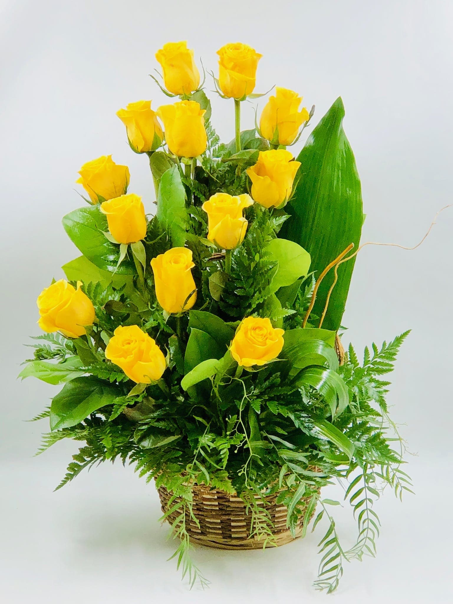 Yellow roses arranged in a woven basket with lush greenery