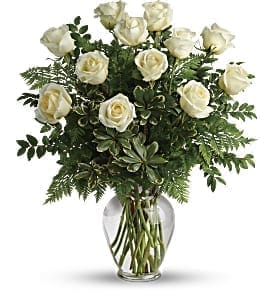 White roses arranged in a clear glass vase with greenery