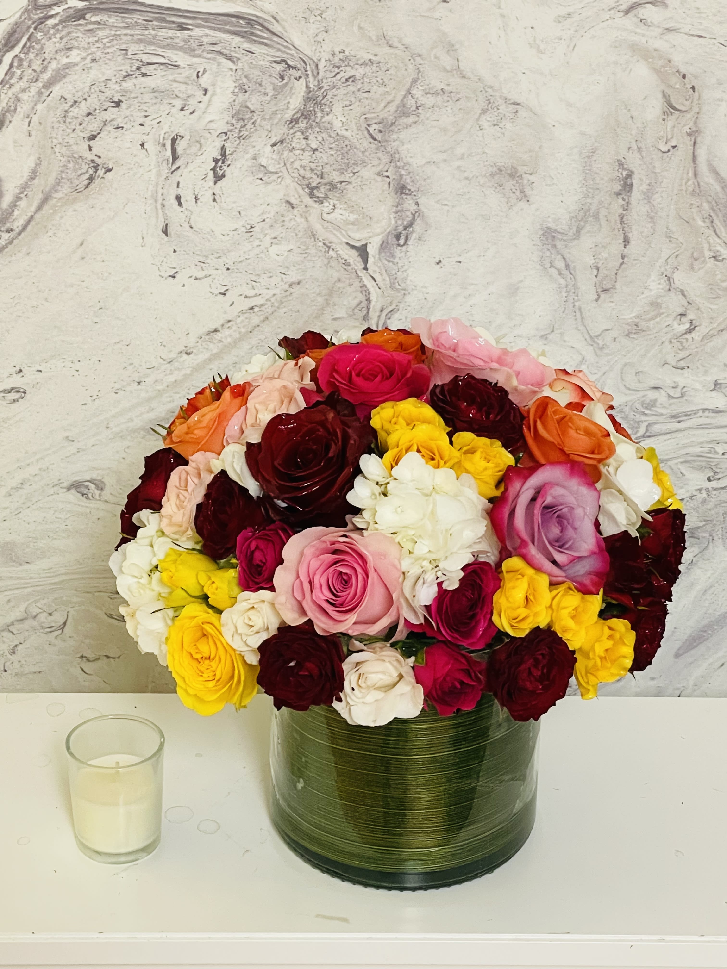 Mixed roses in a green glass vase beside a small candle