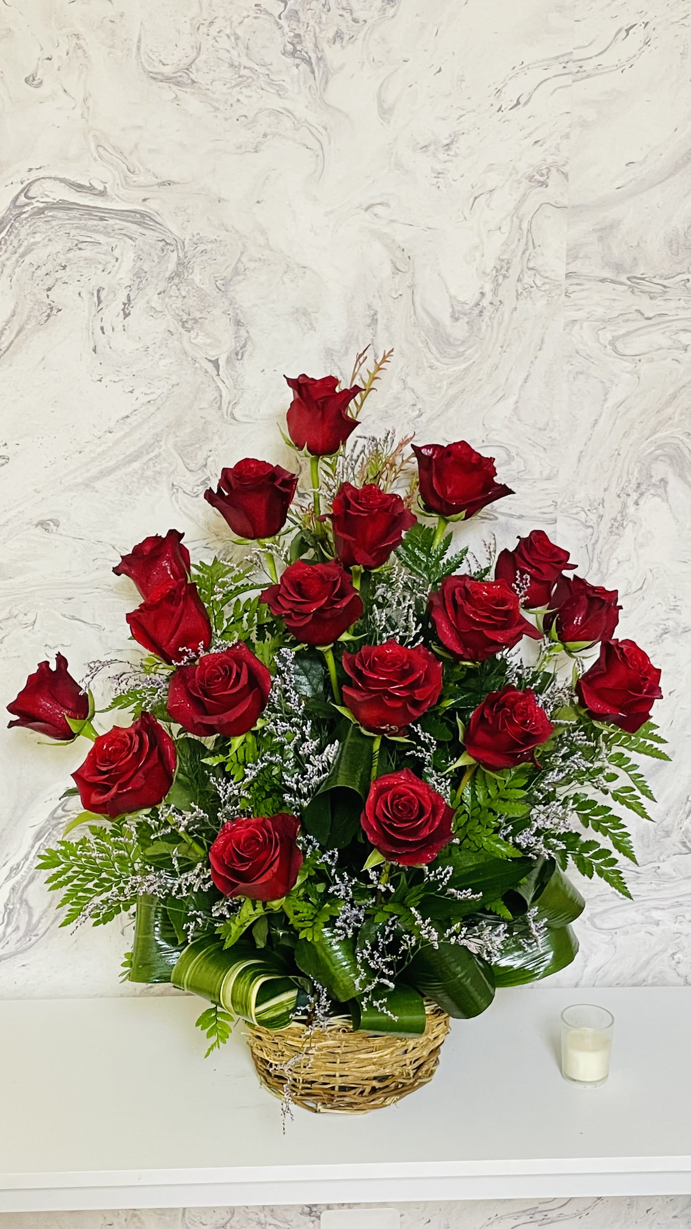 Basket arrangement of red roses with greenery and white filler flowers