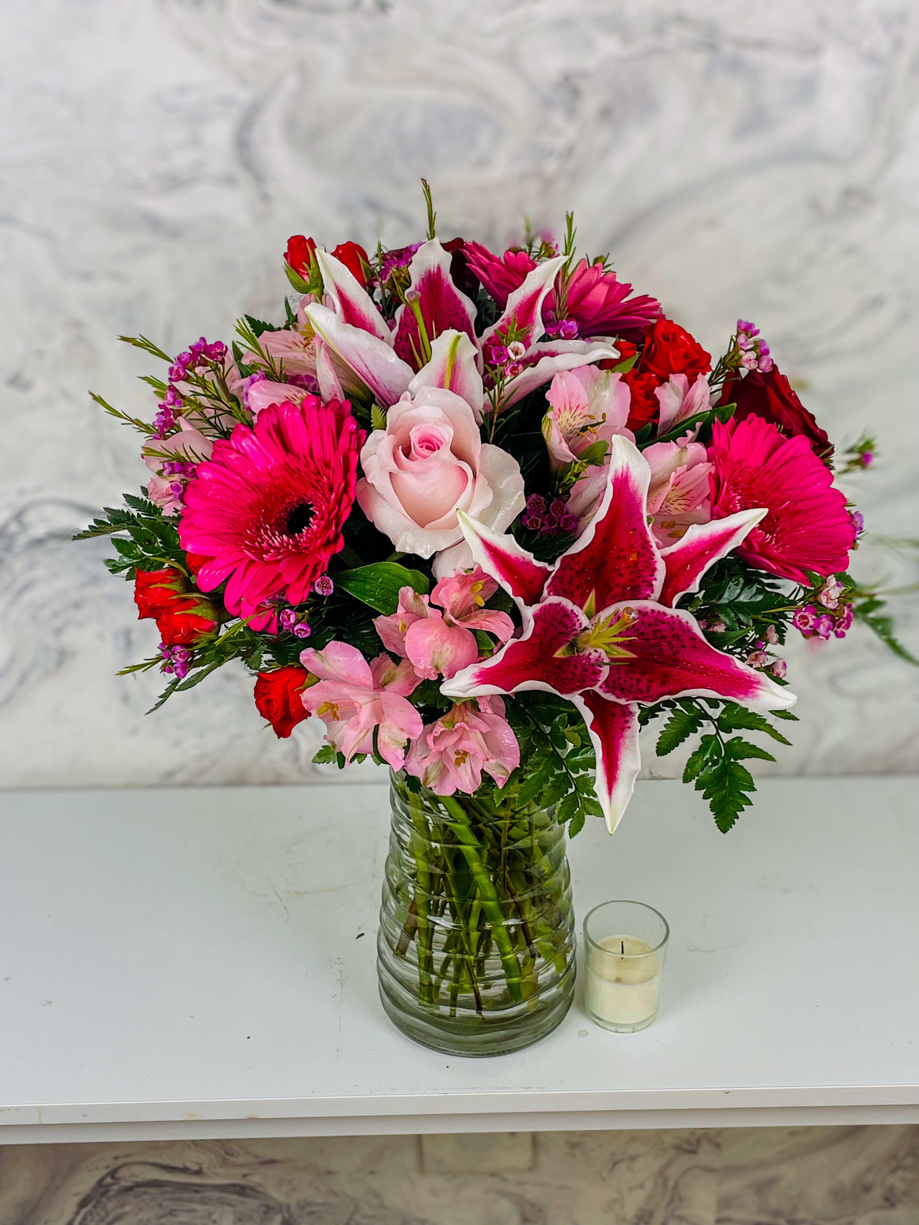 Pink and red mixed bouquet in a glass vase with a small candle beside it