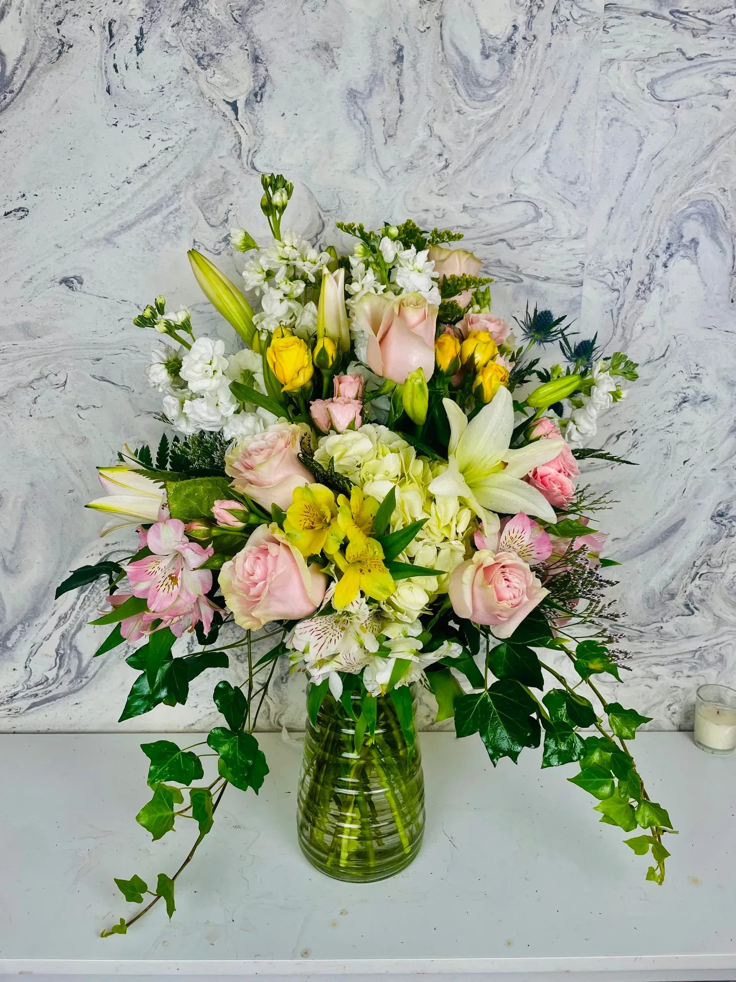 Mixed bouquet of pink roses, white lilies, and yellow flowers in a glass vase