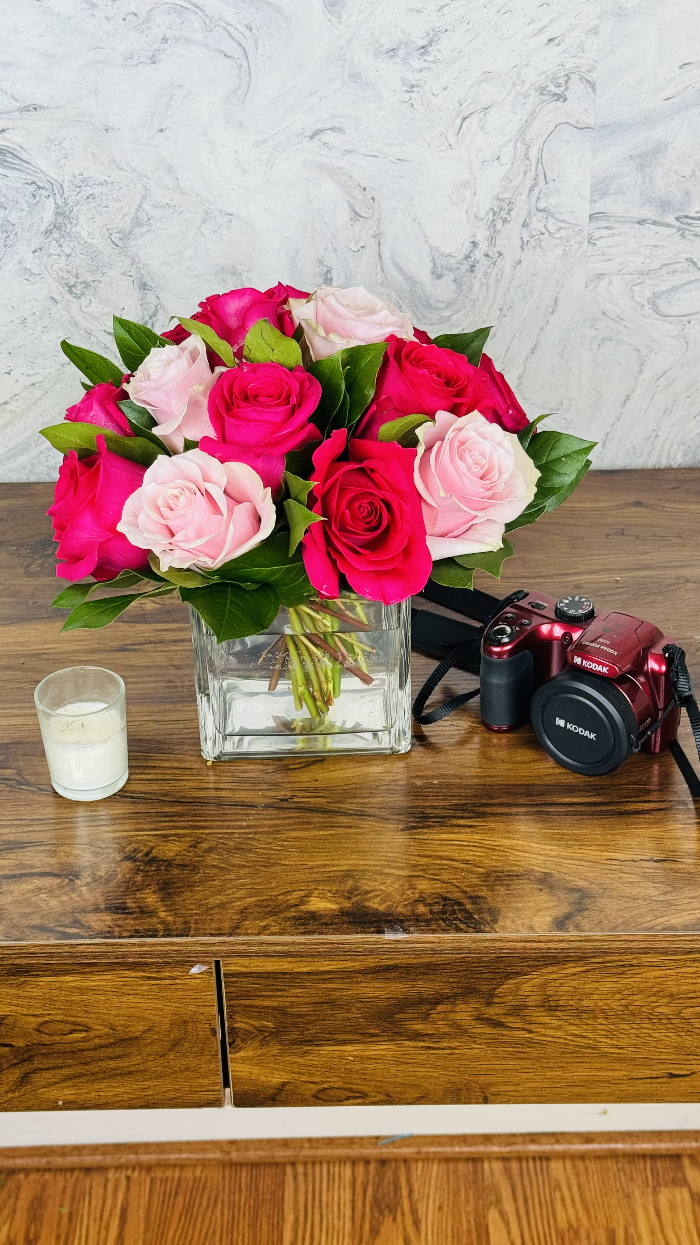 Pink and red roses in a square glass vase on a wooden table