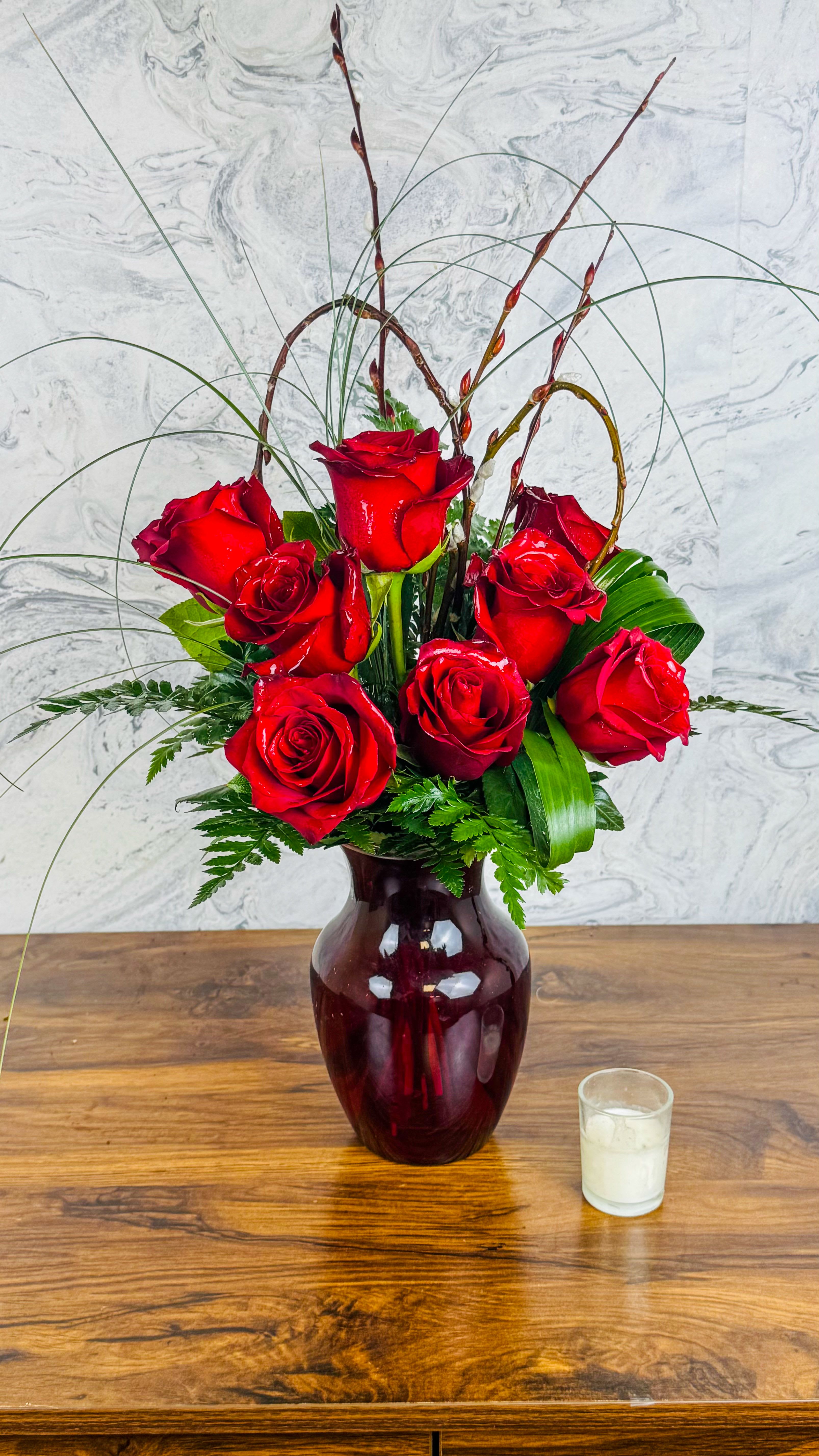 Red roses arranged in a burgundy vase with tall decorative stems