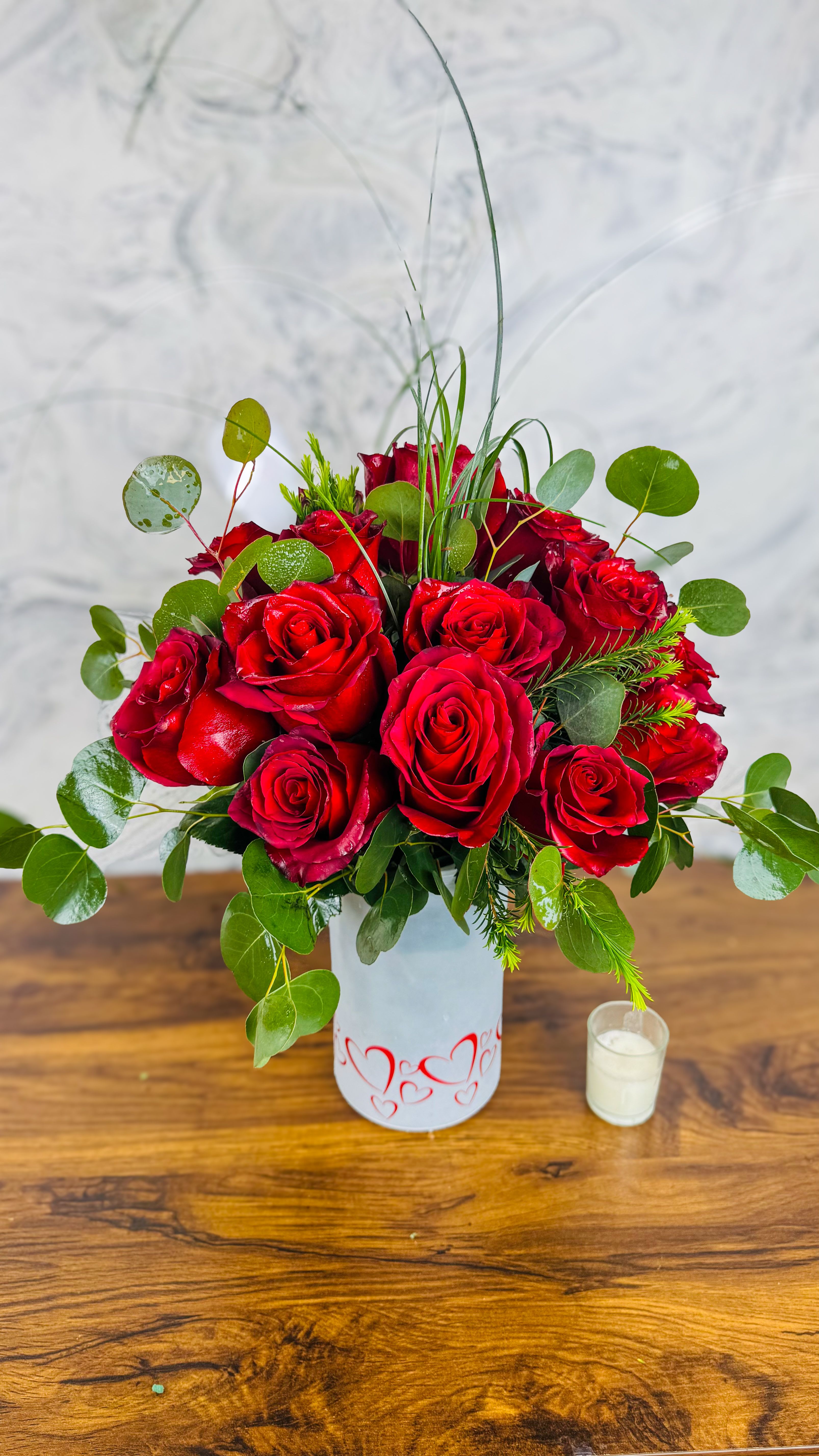 Red roses arranged in a white vase with greenery