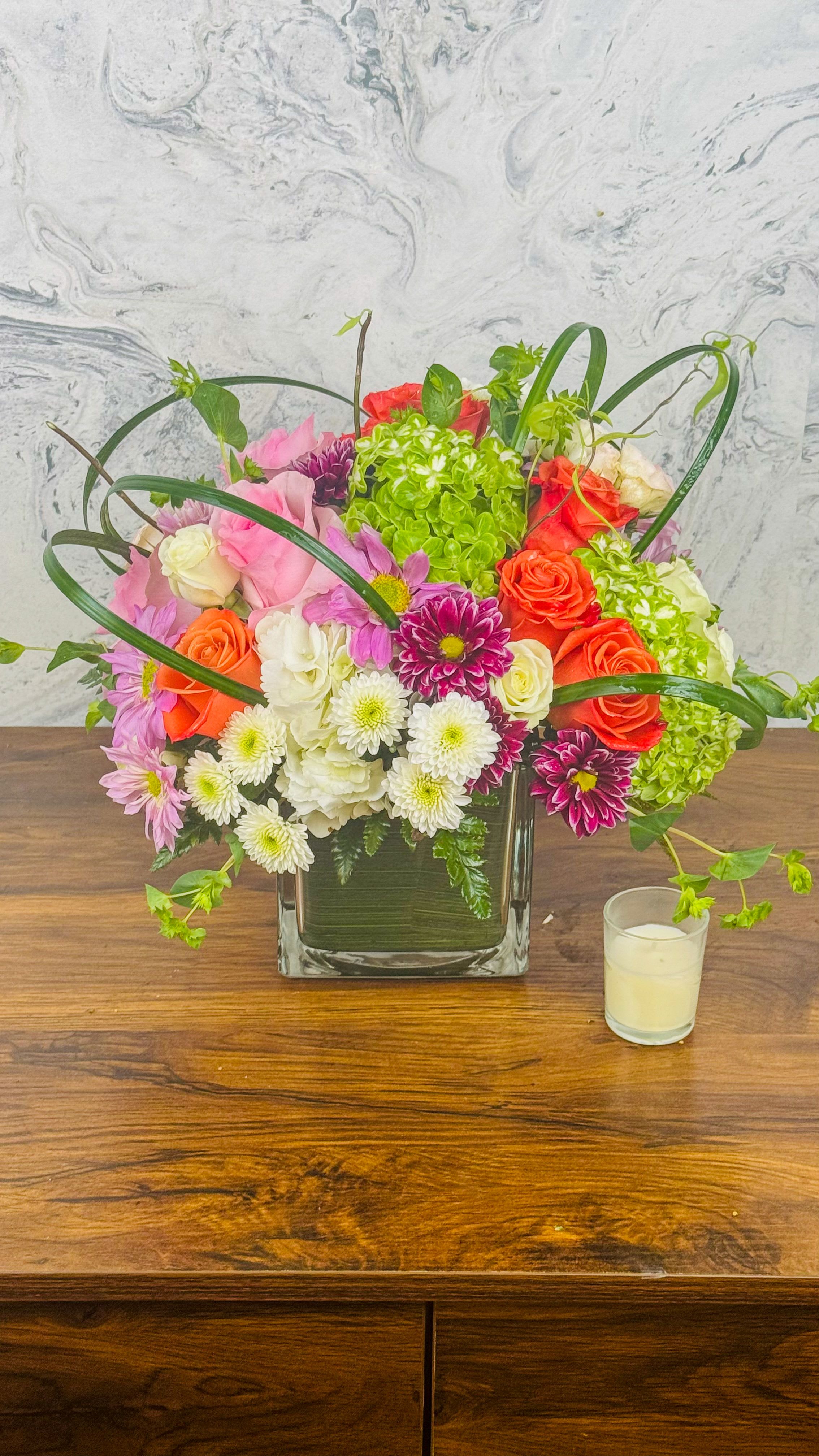 Mixed bouquet of roses, chrysanthemums, and hydrangea in a square glass vase