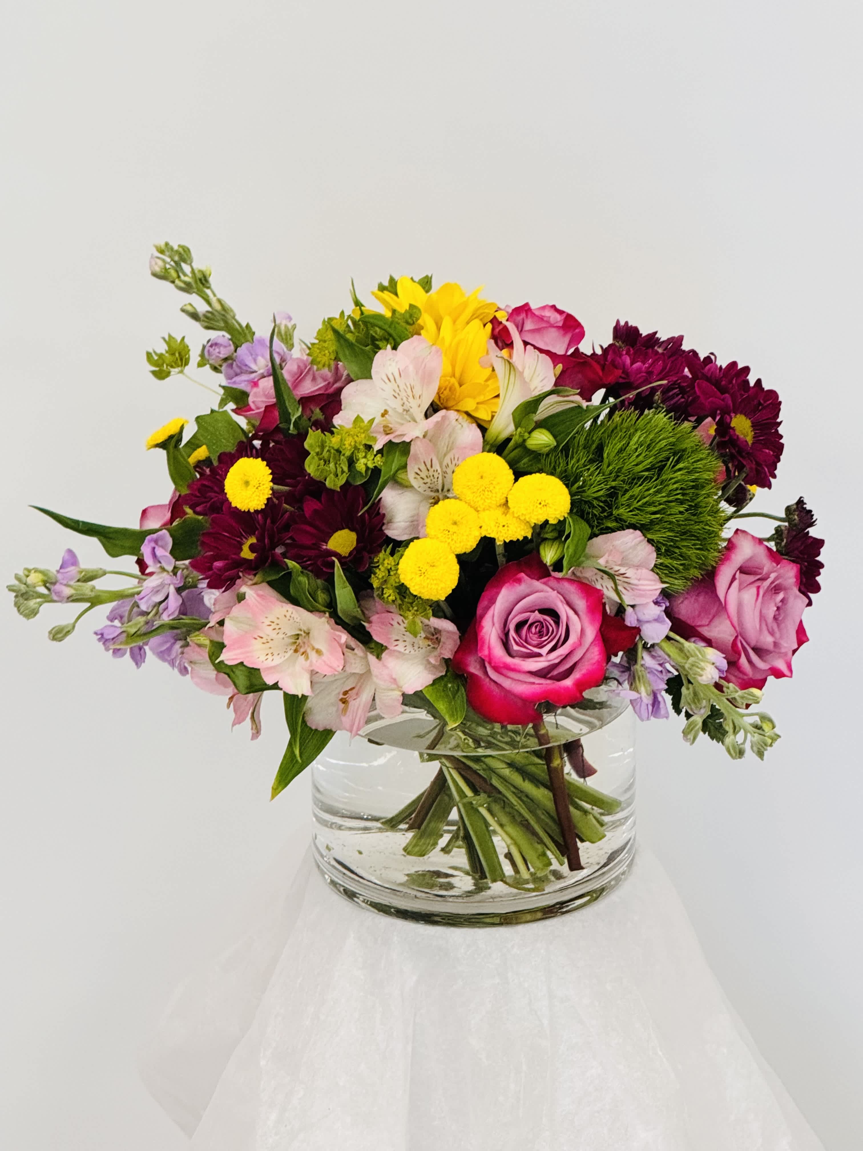Mixed bouquet of pink, yellow, and purple flowers in a clear glass vase