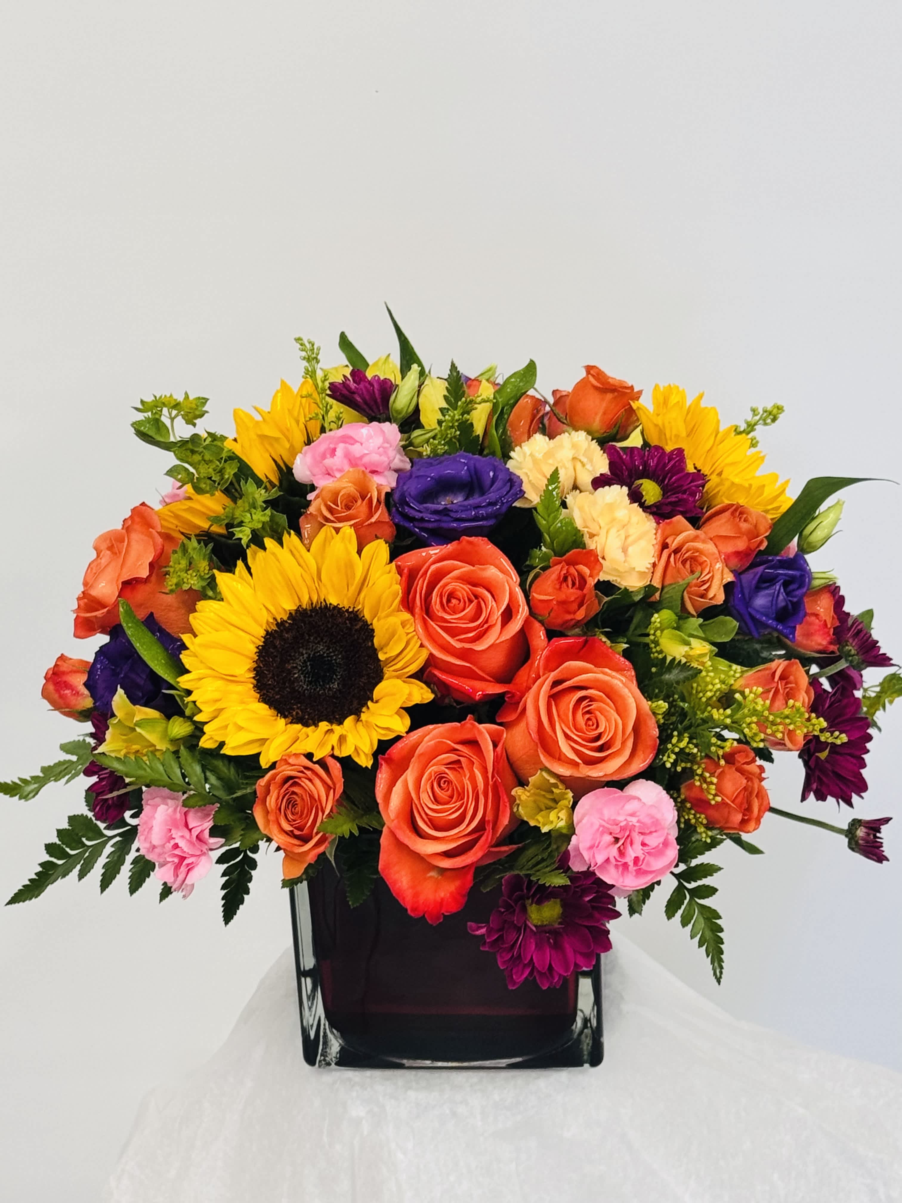 Mixed bouquet with sunflowers, roses, and carnations in a dark vase