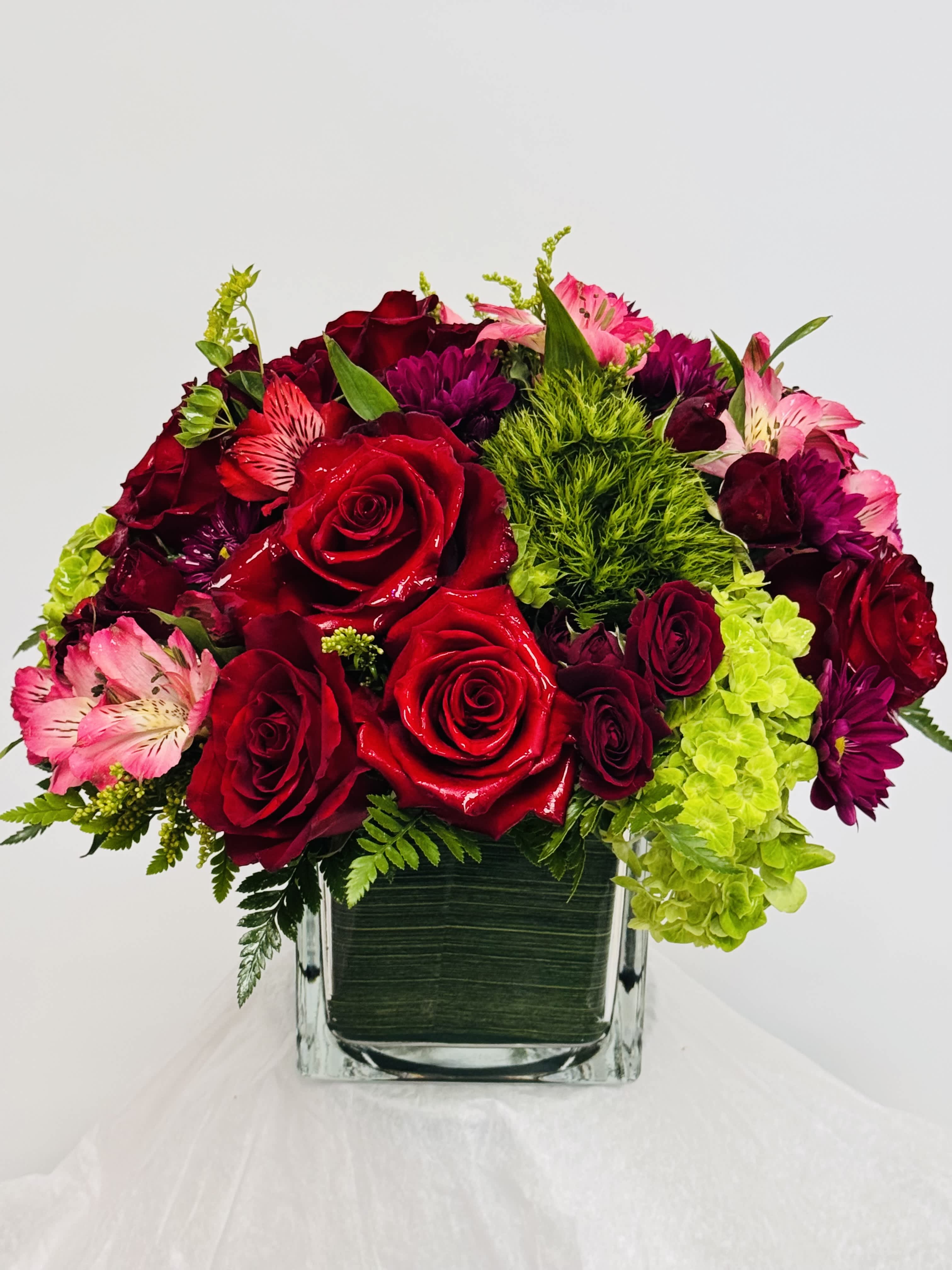 Bouquet of red roses, pink alstroemeria, and purple blooms in a square glass vase