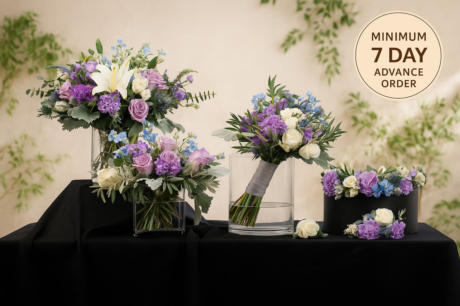 Wedding floral set with purple, white, and blue blooms in glass vases, a bouquet, and a floral crown on black cloth
