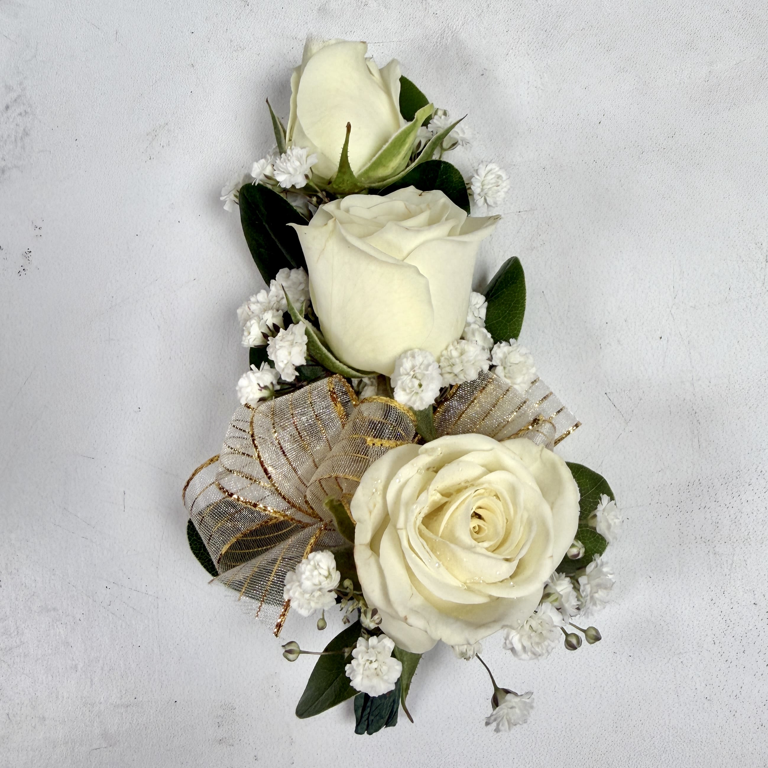 Wrist Corsage with 3 White Spray Roses - This wrist corsage features three white spray roses, babies breath and white and gold sheer ribbon. This choice is a classic pick that matches almost every outfit, and is sure to be a wonderful way to complement a dress for prom or any other fancy occasion. If you want to change the color ribbon, check out our add-ons to pick your desired ribbon color.