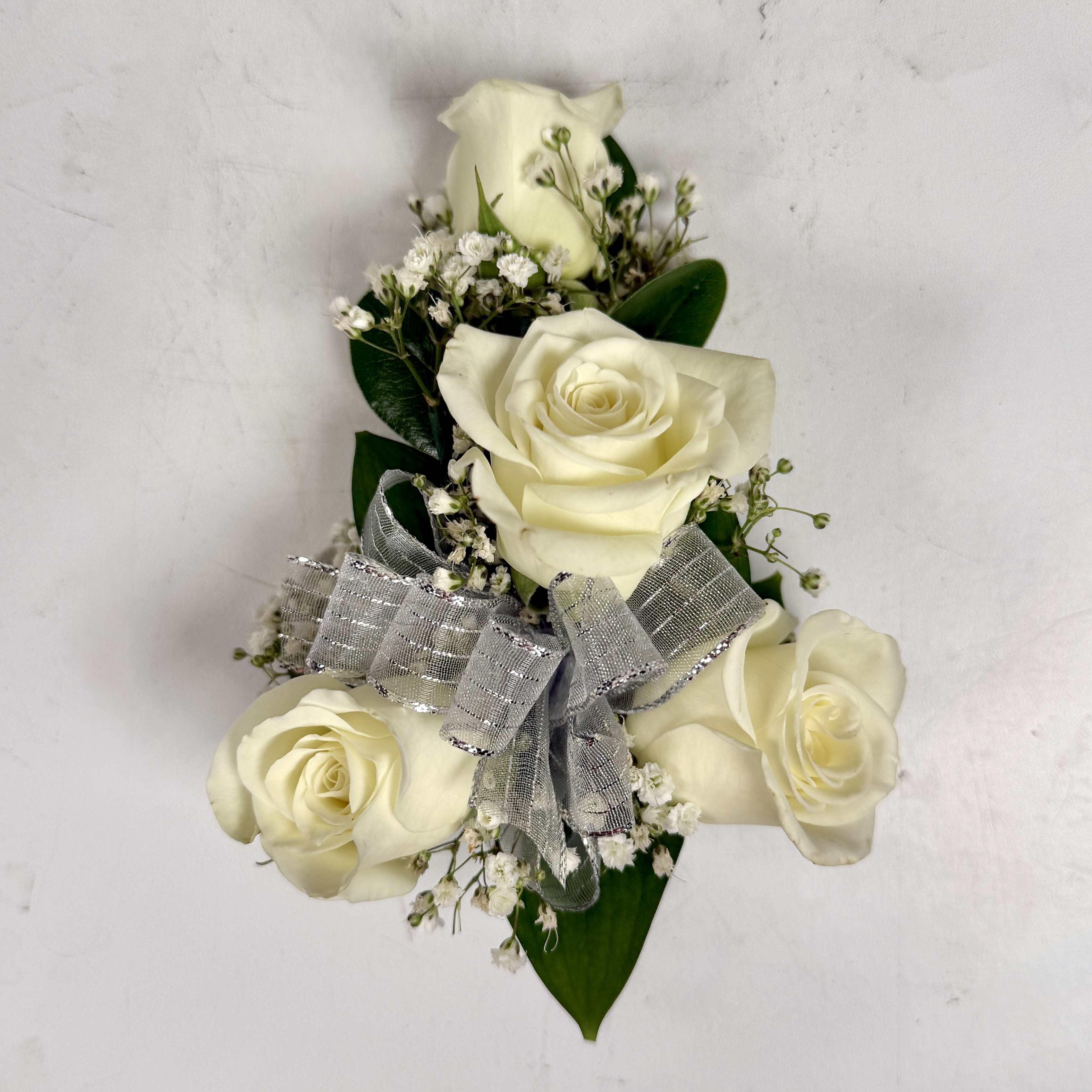 Wrist Corsage with 4 White spray Roses - This wrist corsage features three white spray roses, babies breath and white and silver sheer ribbon. This choice is a classic pick that matches almost every outfit, and is sure to be a wonderful way to complement a dress for prom or any other fancy occasion. If you want to change the color ribbon, check out our add-ons to pick your desired ribbon color.