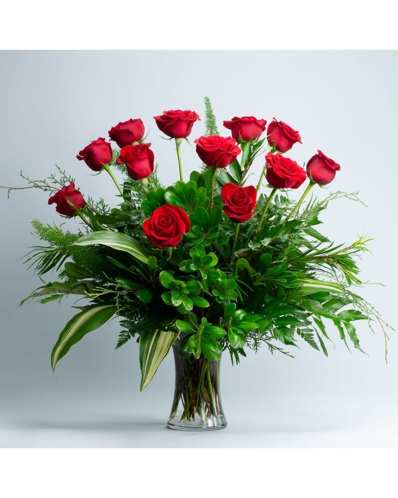 Red roses arranged in a clear glass vase with lush greenery