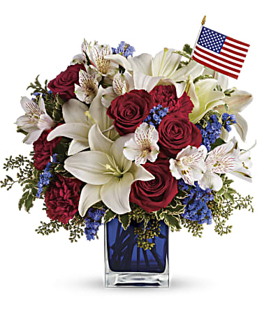 Red roses and white lilies in a blue glass vase with a small American flag