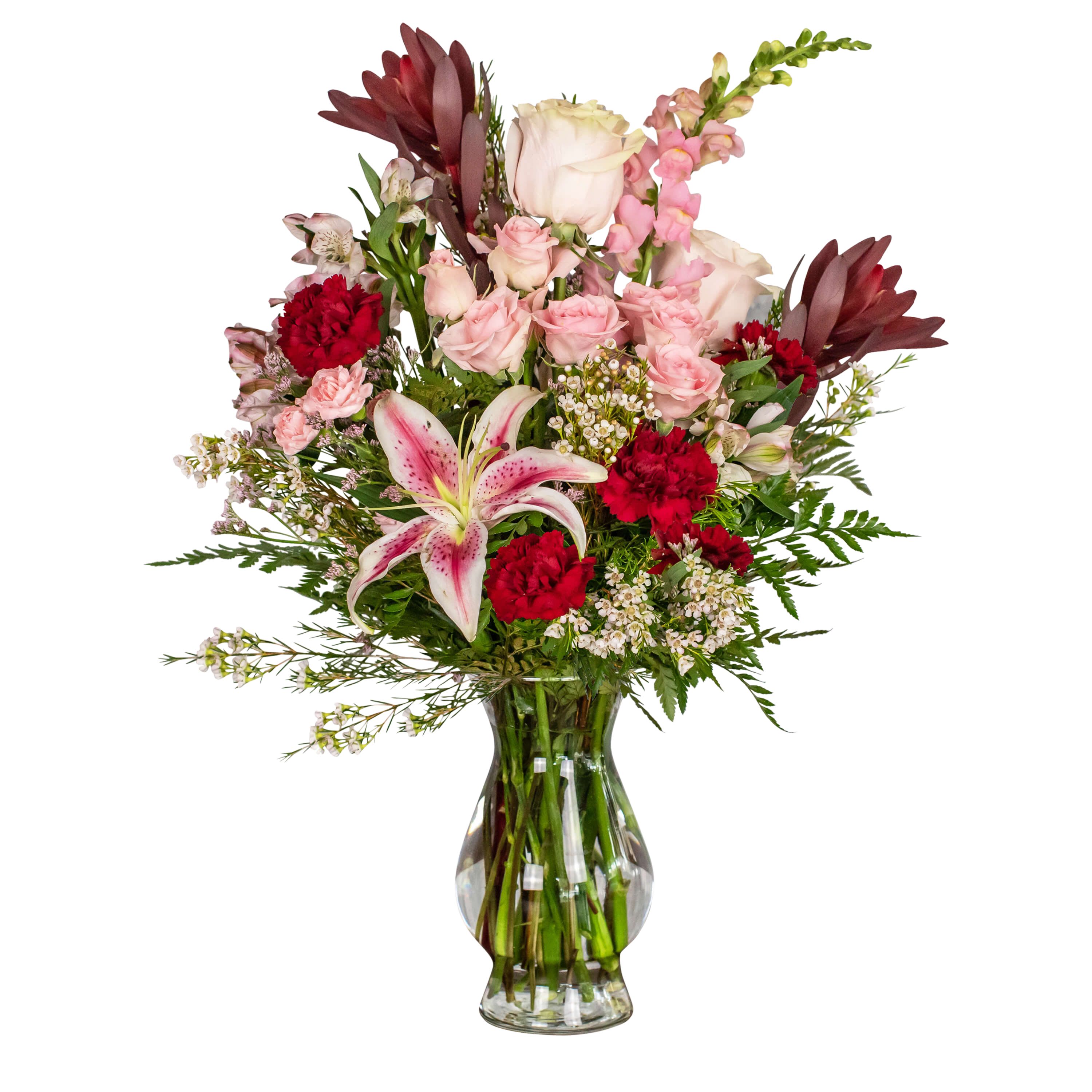 Mixed bouquet of pink roses, red carnations, and a pink lily in a glass vase.