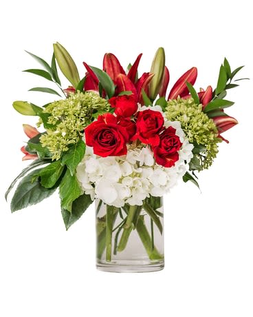 Red roses and lilies arranged with white hydrangeas in a glass vase