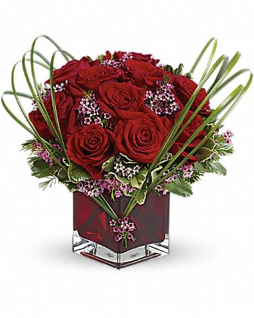 Red roses arranged in a square glass vase with looping grass accents