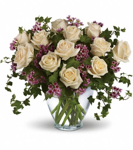 The Elegant  - Romance blossoms beautifully within this elegant bouquet. The serenity and innocence of cream-colored roses is in delightful juxtaposition with lavender wax flower and fresh ivy greens. It's as romantic as a stroll through the English countryside. A dozen crème roses lavender wax flower and ivy are perfectly arranged in a serenity glass vase. Approximately 17" W x 15" H Orientation: All-Around As Shown : DG69-1A