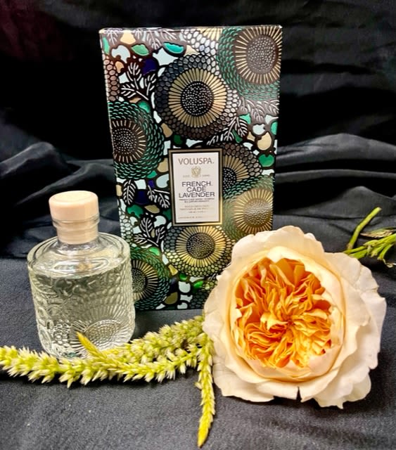 Perfume bottle, floral candle box, and a peach rose on dark fabric