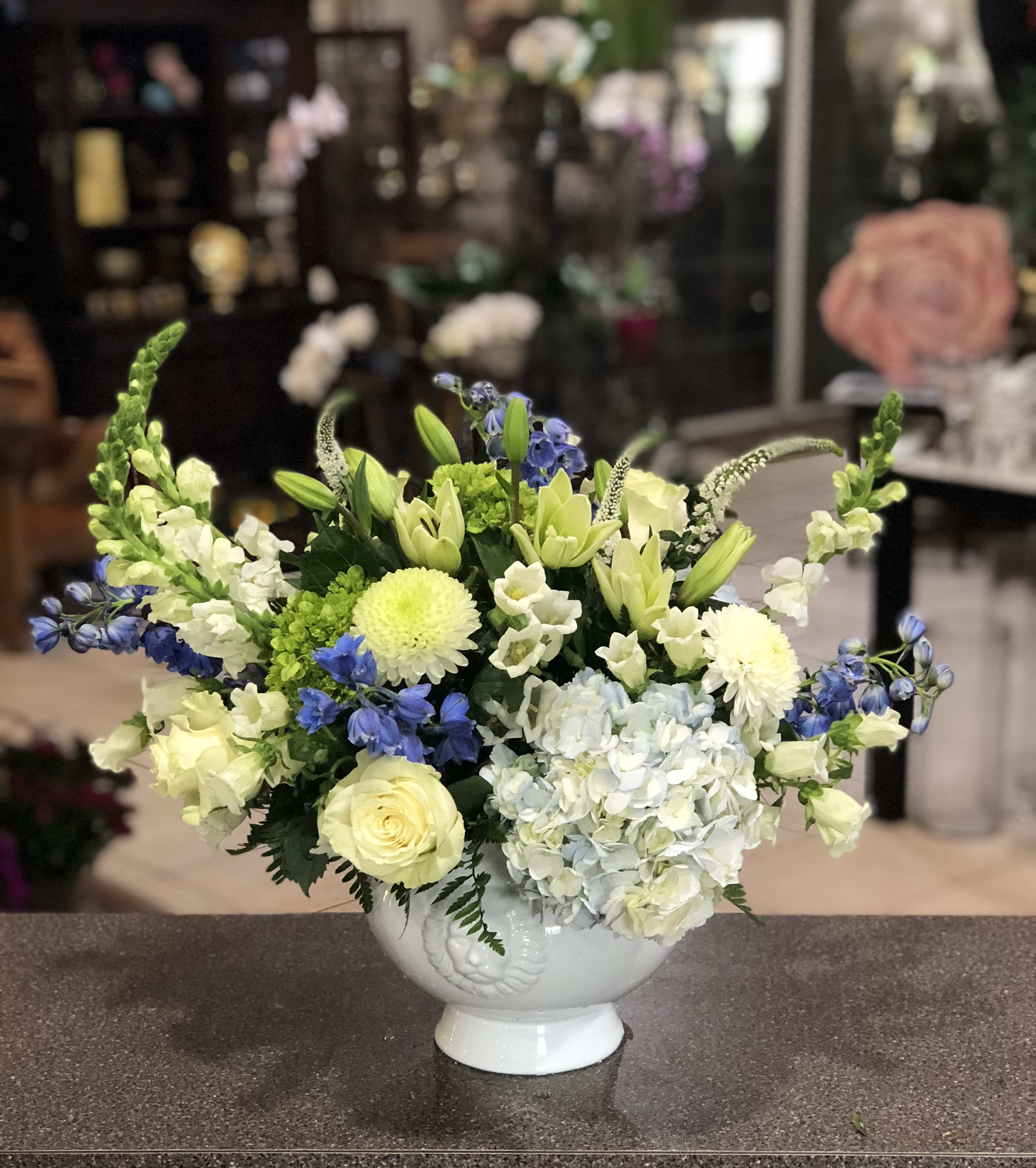 Mixed floral arrangement in a white pedestal vase with pale yellow, white, blue, and green blooms