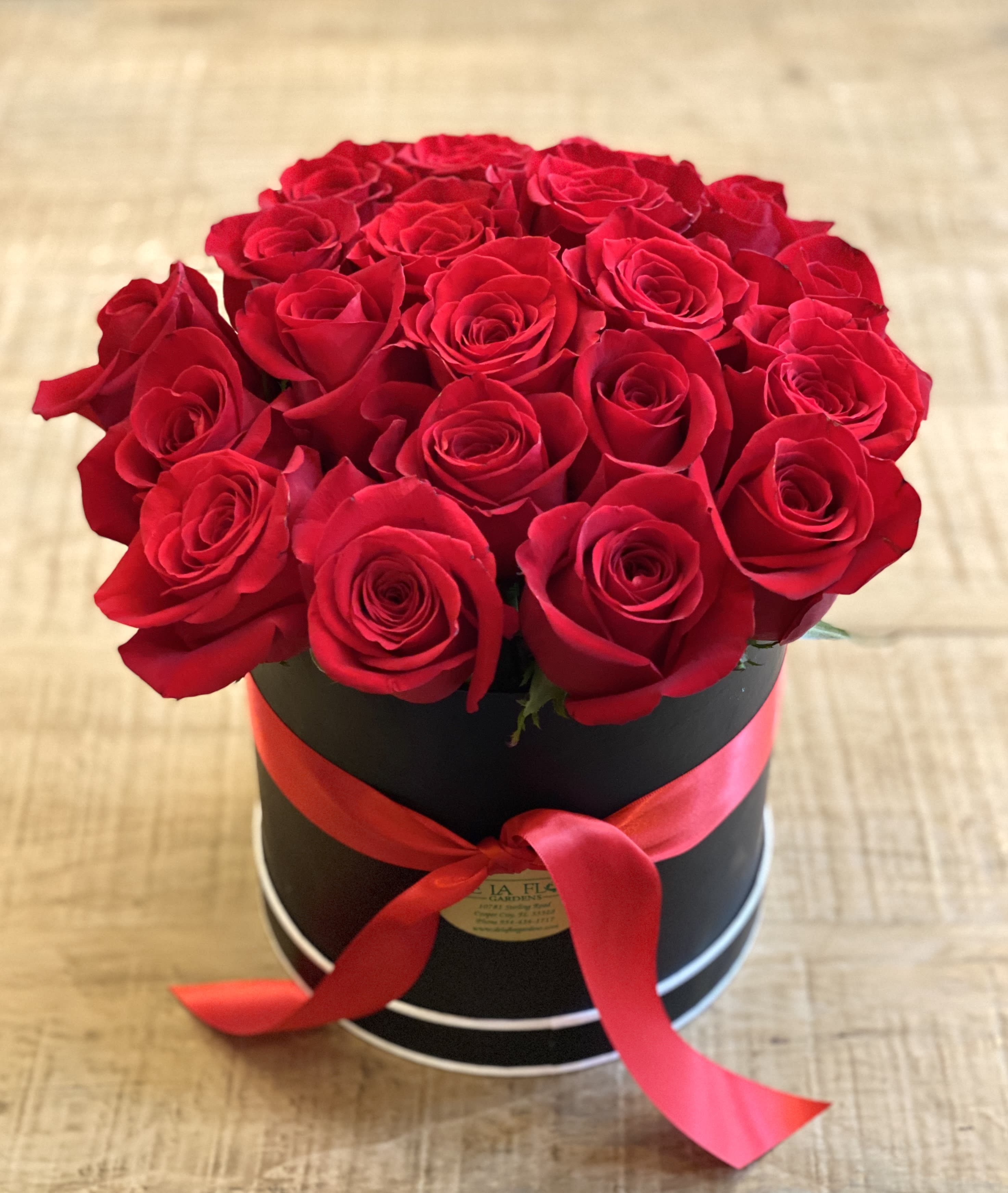 Red roses arranged in a black round box with a red ribbon
