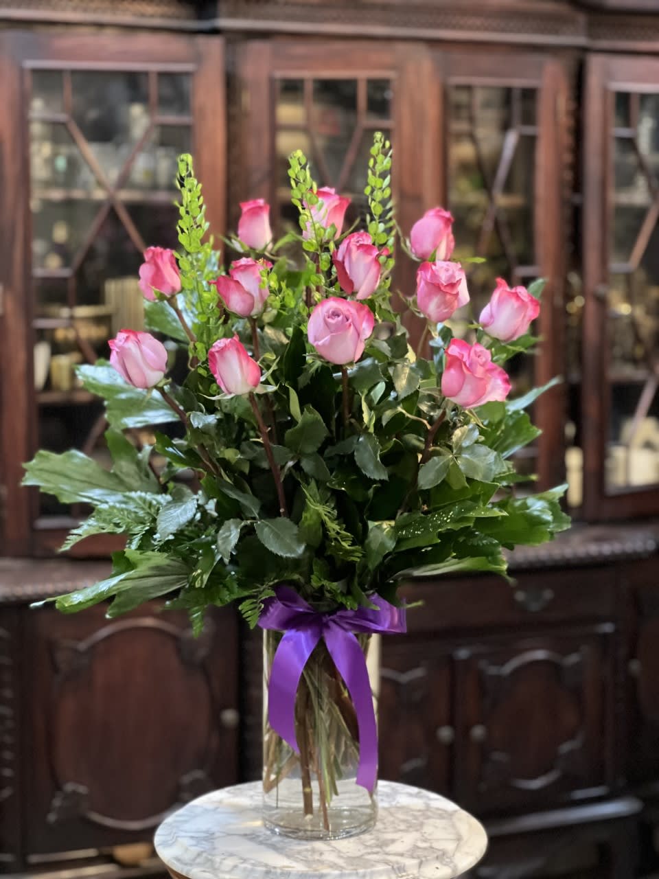 Pink roses in a clear glass vase with a purple ribbon