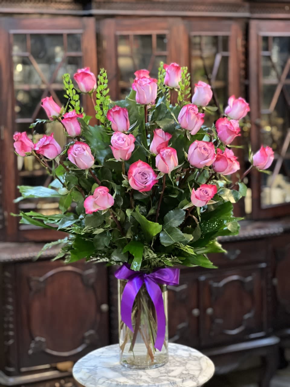 Pink roses arranged in a clear glass vase with a purple ribbon