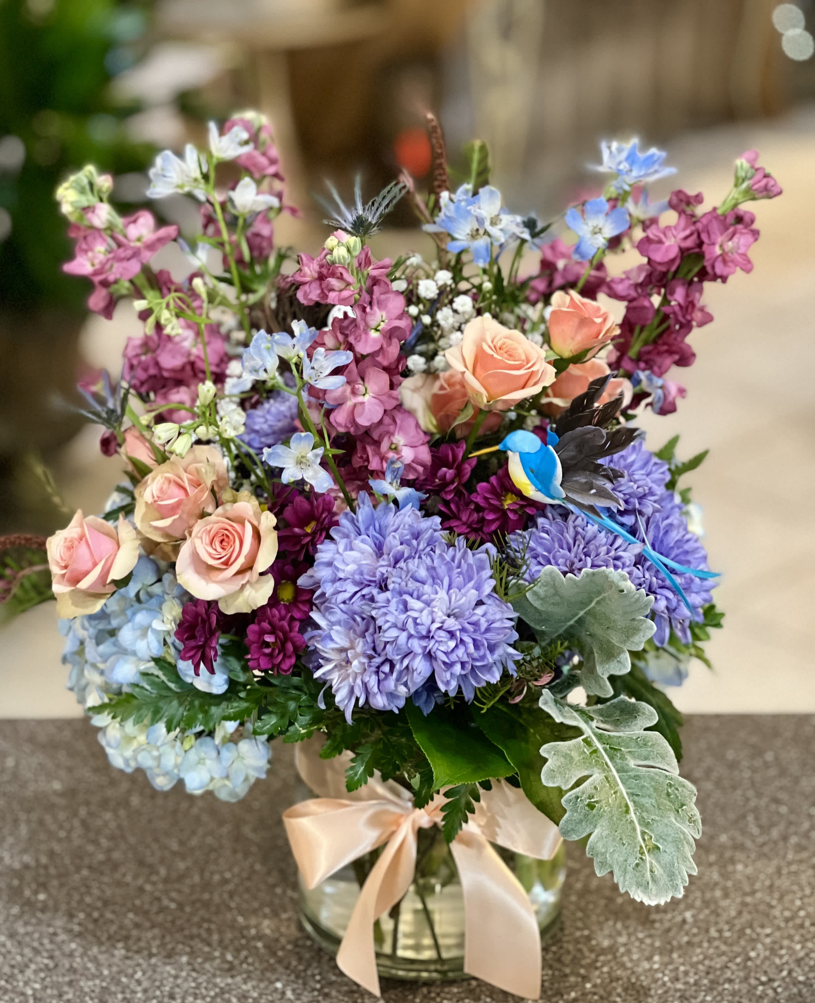 Mixed bouquet of pastel roses, purple blooms, and blue flowers in a glass vase