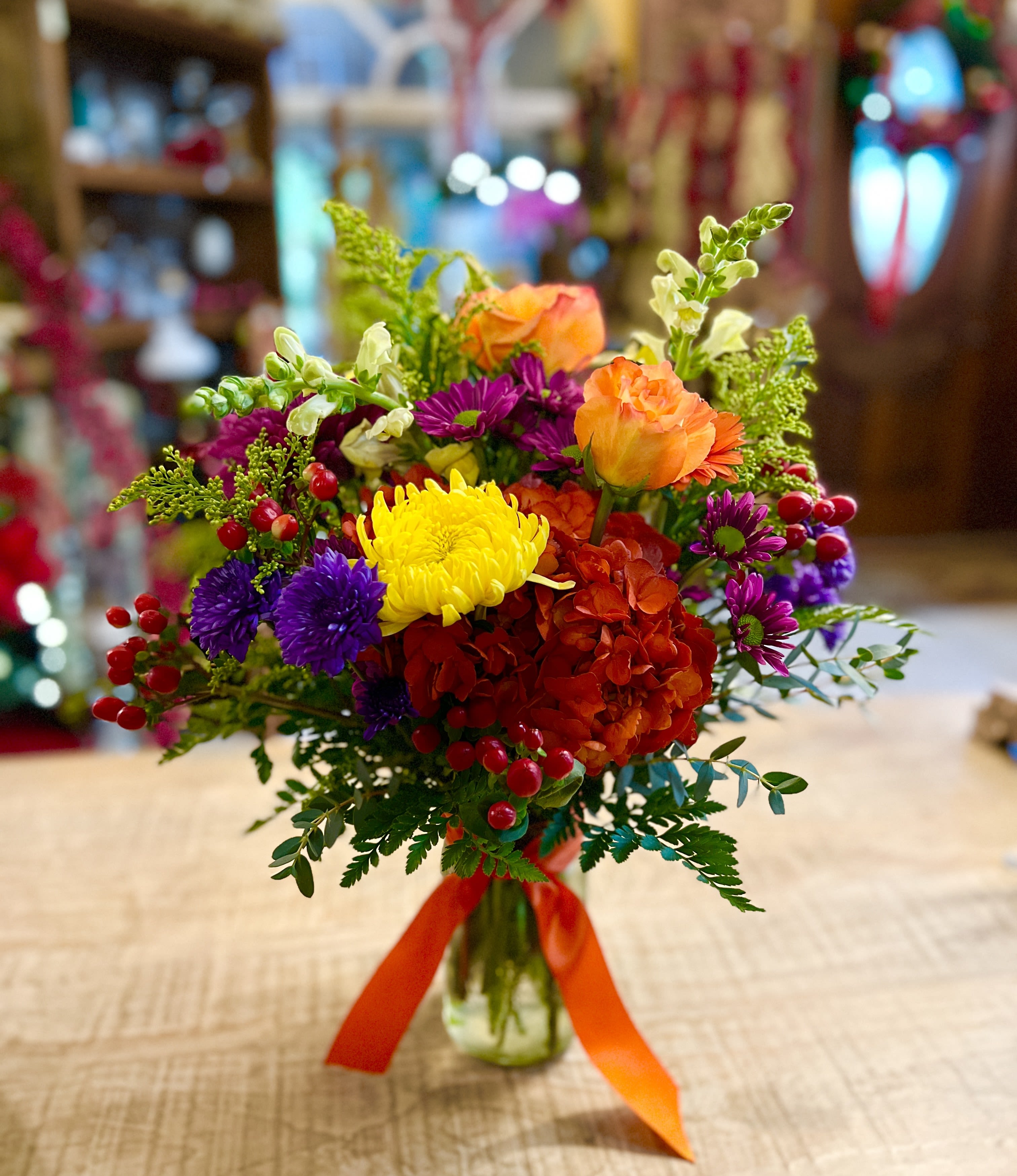 Colorful mixed bouquet in a glass vase with orange, yellow, purple, and red blooms
