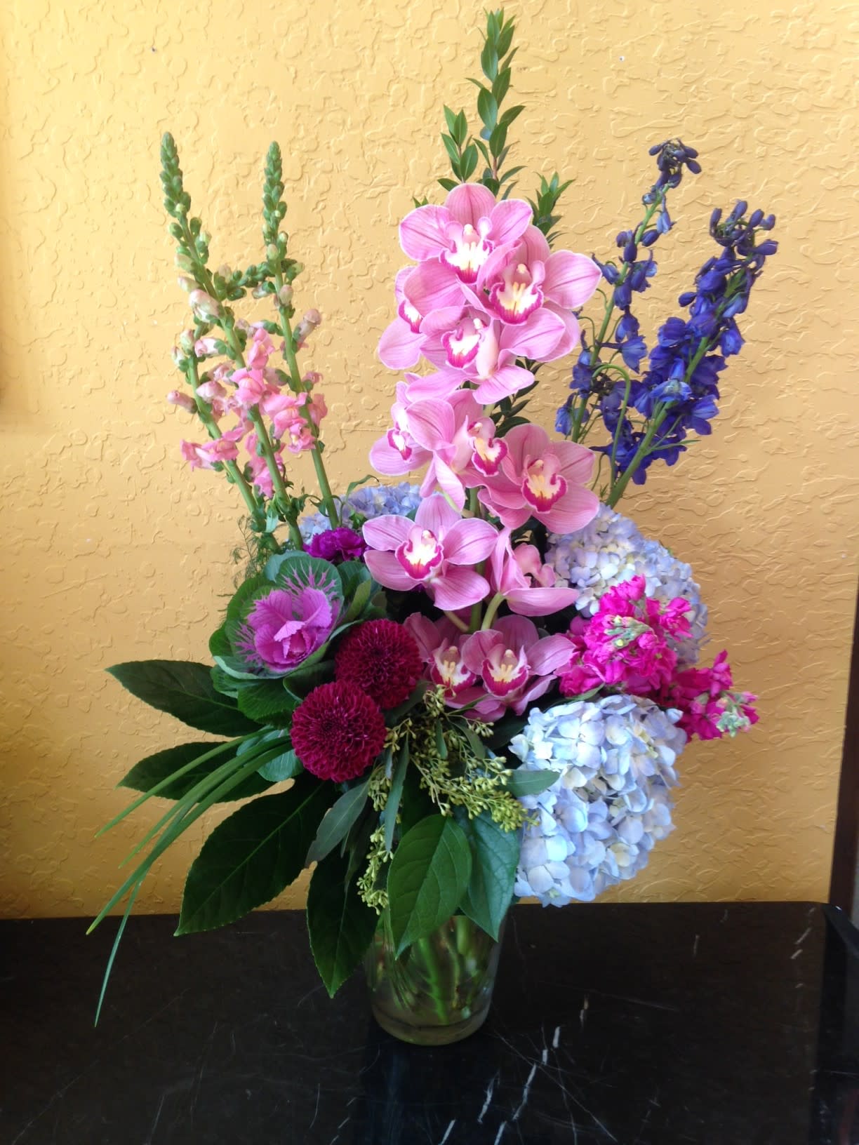 Tall bouquet of pink orchids and blue hydrangeas in a glass vase