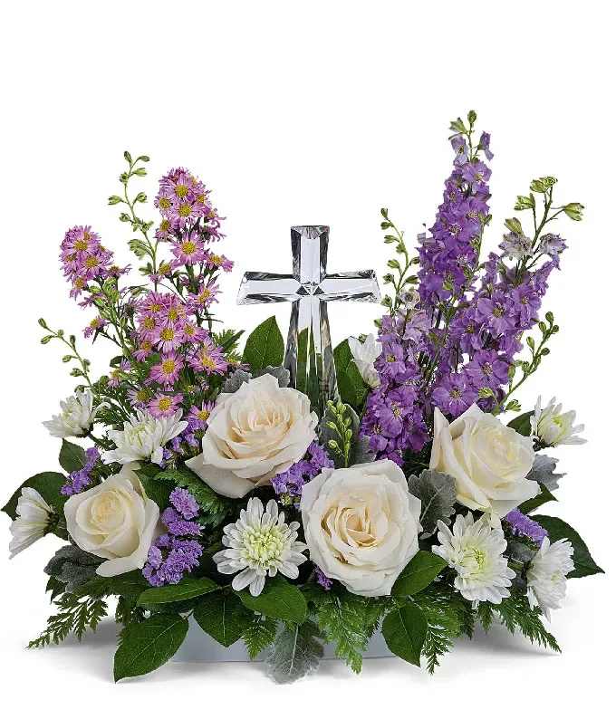 Cruz Cristal - Graceful Cross Sympathy Arrangement  Honor the memory of a loved one with this elegant sympathy floral arrangement, thoughtfully designed around a beautiful silver cross. Featuring a harmonious blend of peach roses, spray roses, alstroemeria, carnations, and seasonal blooms, this arrangement offers a heartfelt expression of peace, comfort, and everlasting love.  Perfect for funeral services, memorials, churches, or sending your deepest condolences to family and friends. Each arrangement is handcrafted by our expert florists using only the freshest, highest-quality flowers.  Please Note: Flower varieties and greenery may vary based on seasonal availability while maintaining the overall style, color palette, and premium quality of the design.