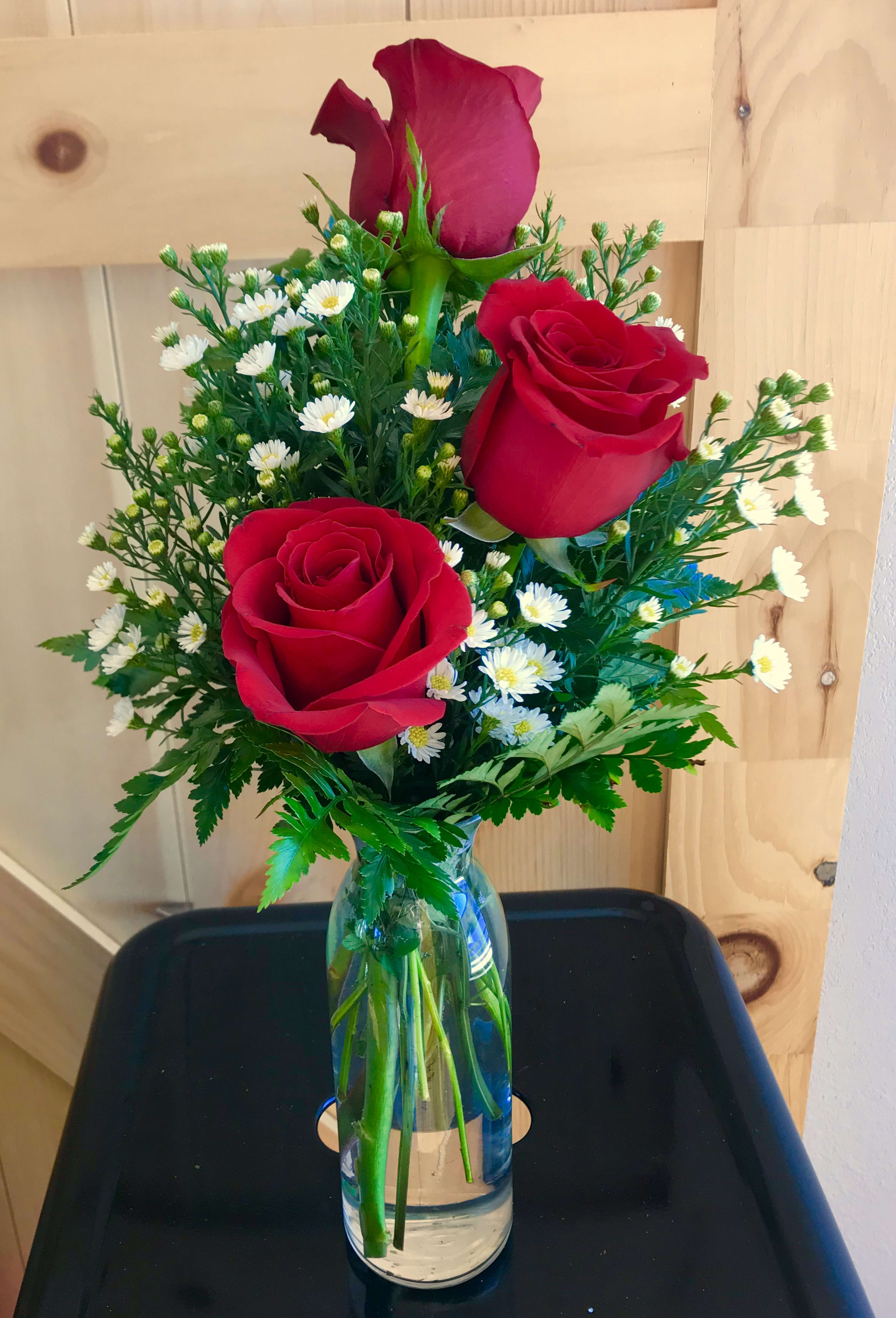 Three red roses with small white daisies in a glass vase