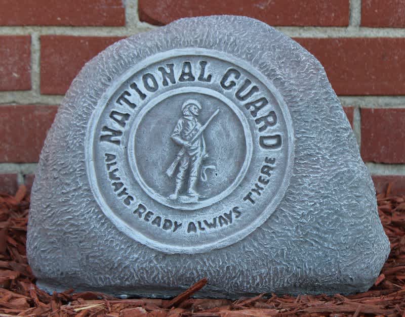 Gray memorial stone with a National Guard emblem against a brick wall