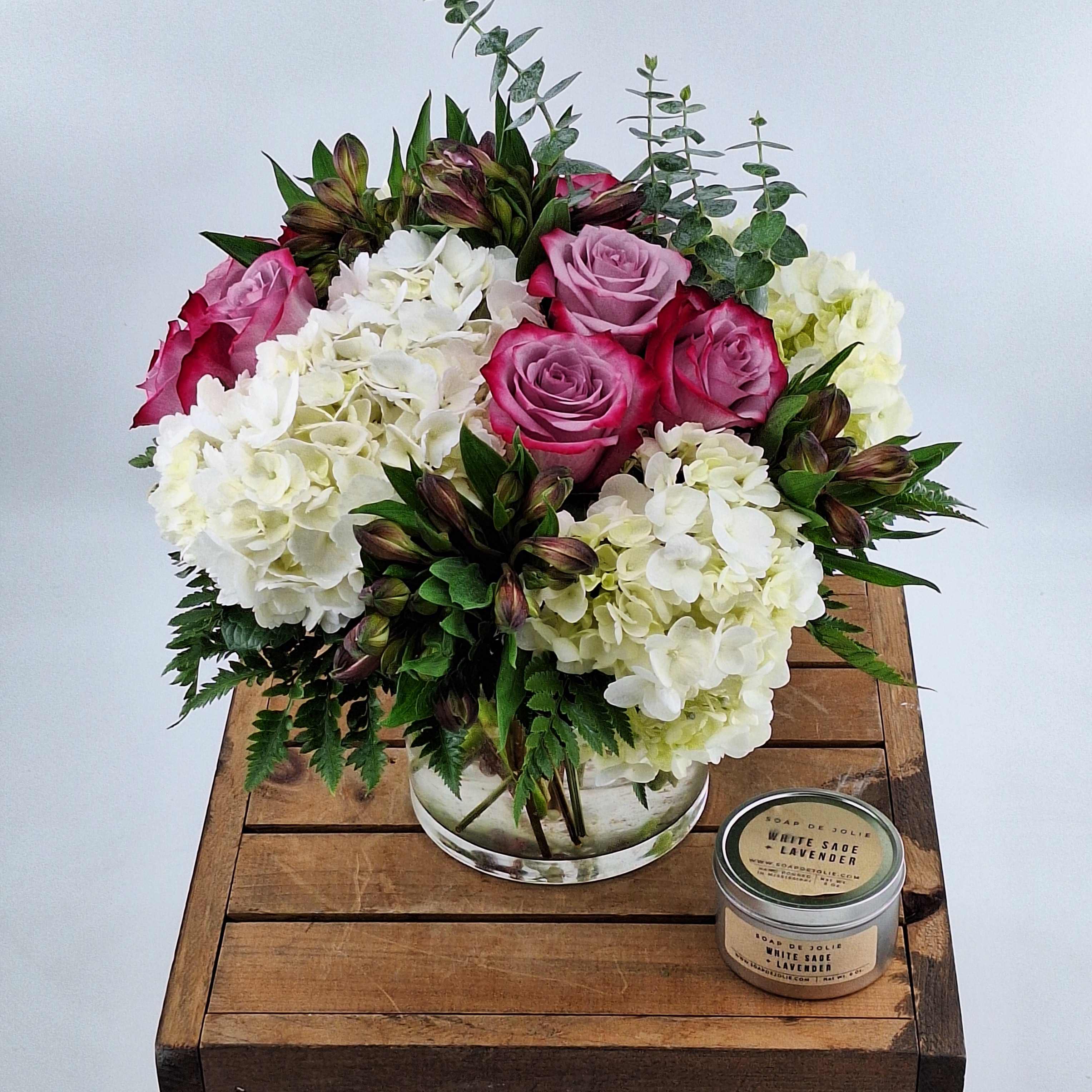 Pink roses and white hydrangeas in a glass vase with a small candle beside it