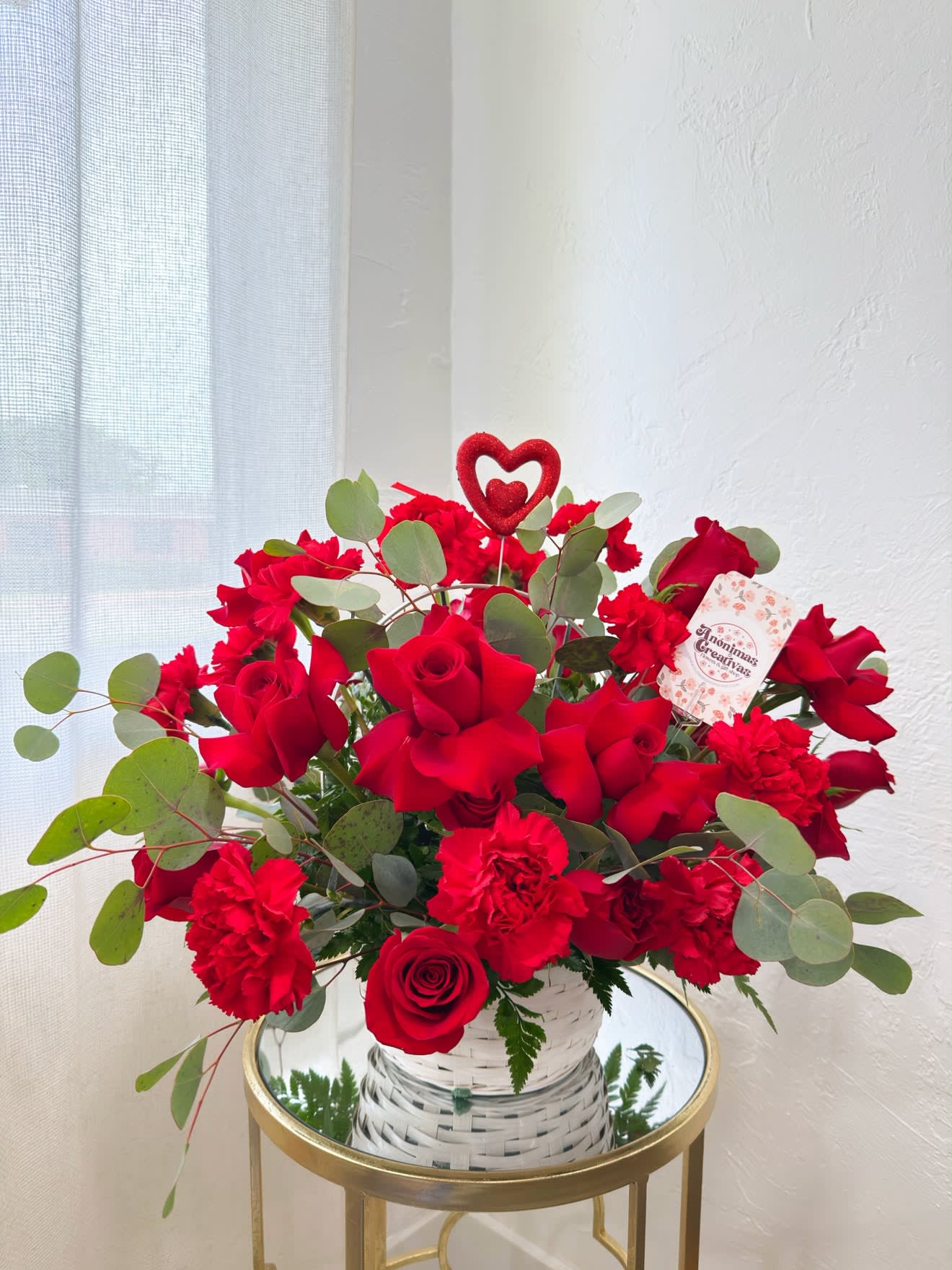 Red roses and carnations in a white woven vase with a heart pick
