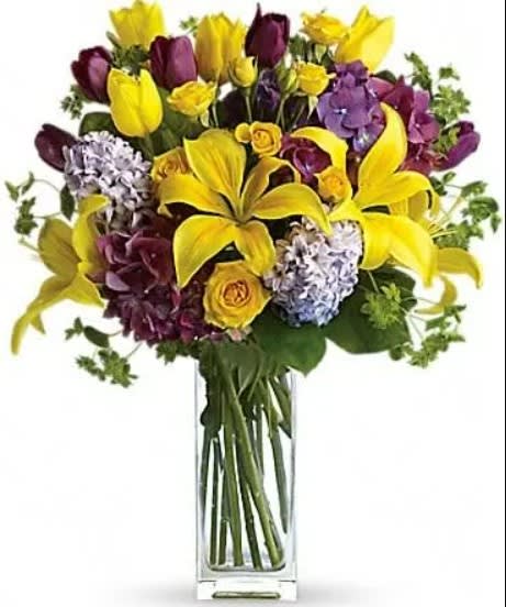 Yellow lilies and purple flowers in a clear glass vase