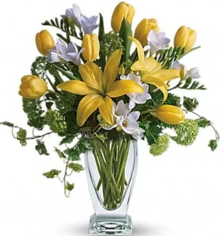 Yellow tulips and pale lavender flowers in a clear glass vase