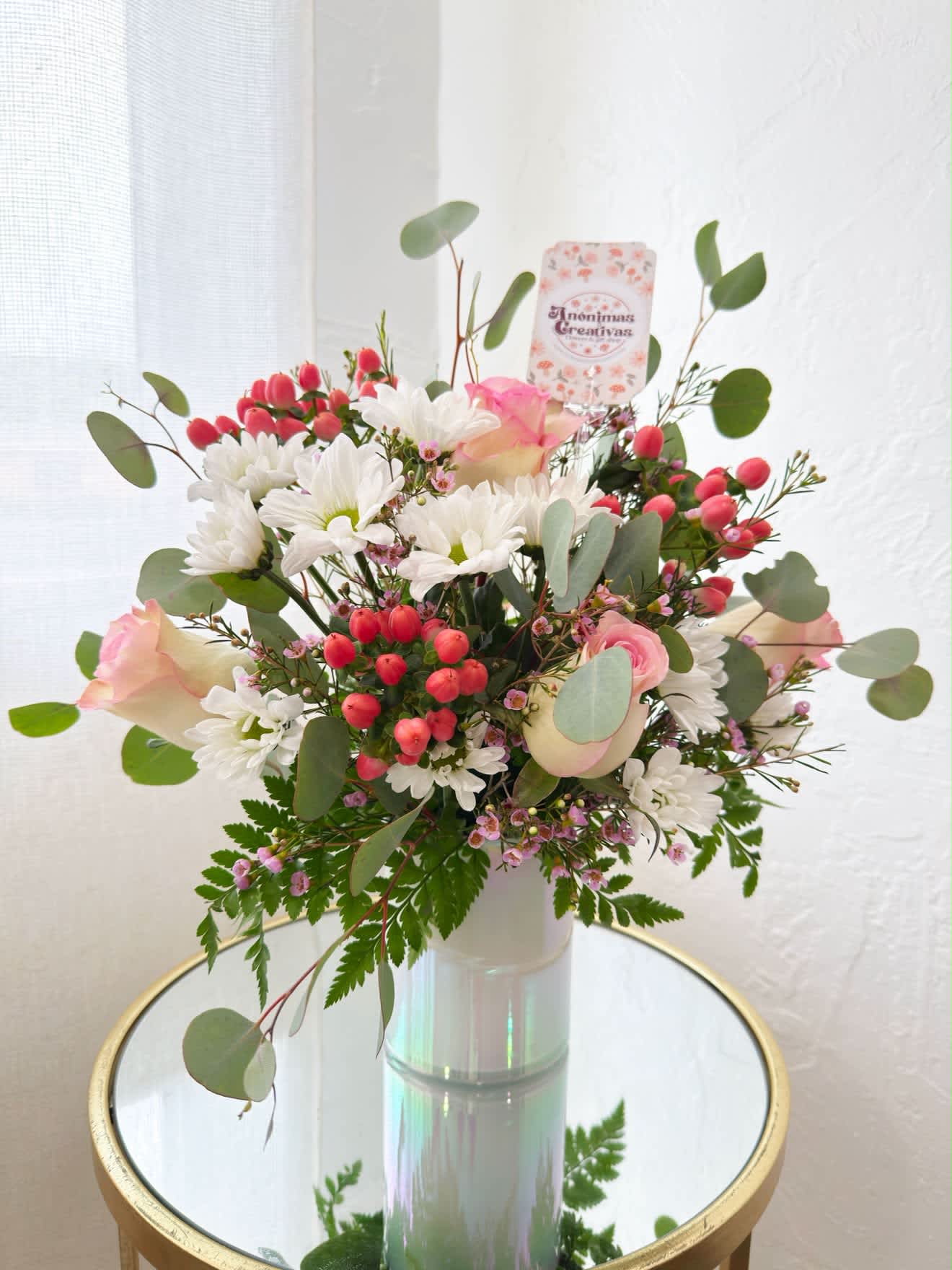 Bouquet of white daisies, pink roses, and red berries in a glass vase