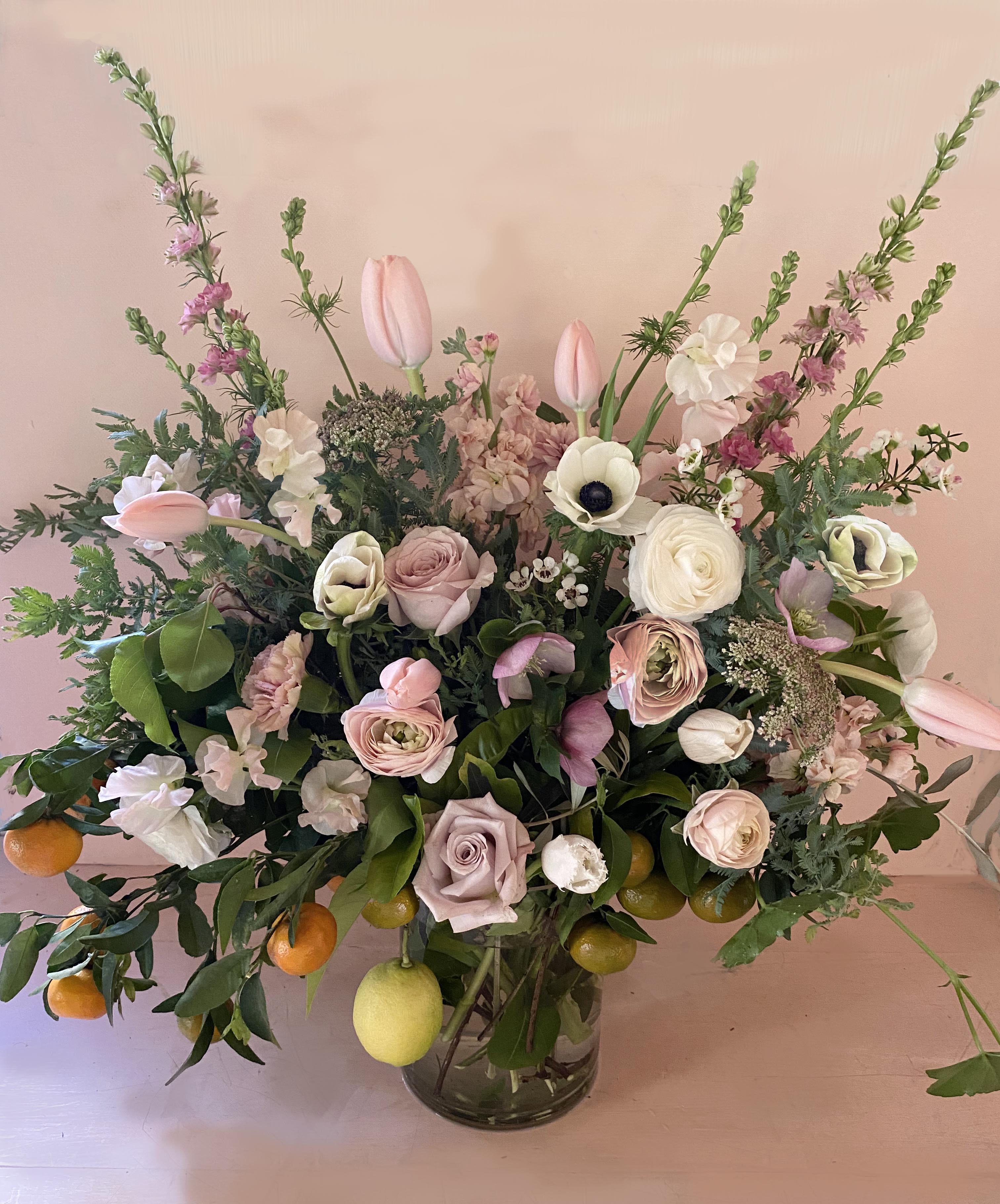 The Winona wild - Gorgeous, tall, fresh, natural and wild. This lush creation will make a beautiful statement, freshen up the hallway, look pretty in the kitchen, bring joy to a loved one - it is definetely a show stopper. Made of seasonal fresh, green branches and coral/white/pastel stems with overflowing vibes. Very California.  Arrangement measures appx 25" weide and tall. placed in a clear cylinder vase.