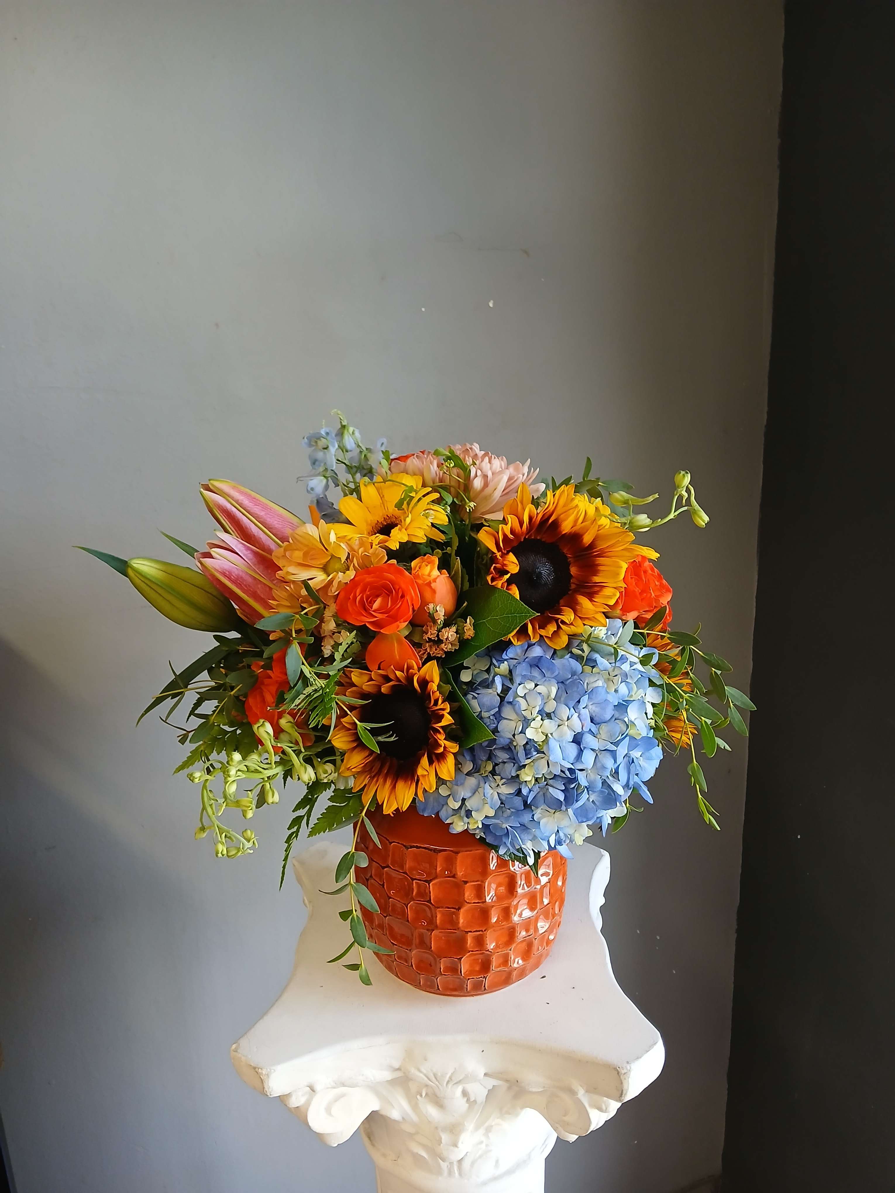 Colorful mixed bouquet in an orange textured vase with sunflowers and blue hydrangea