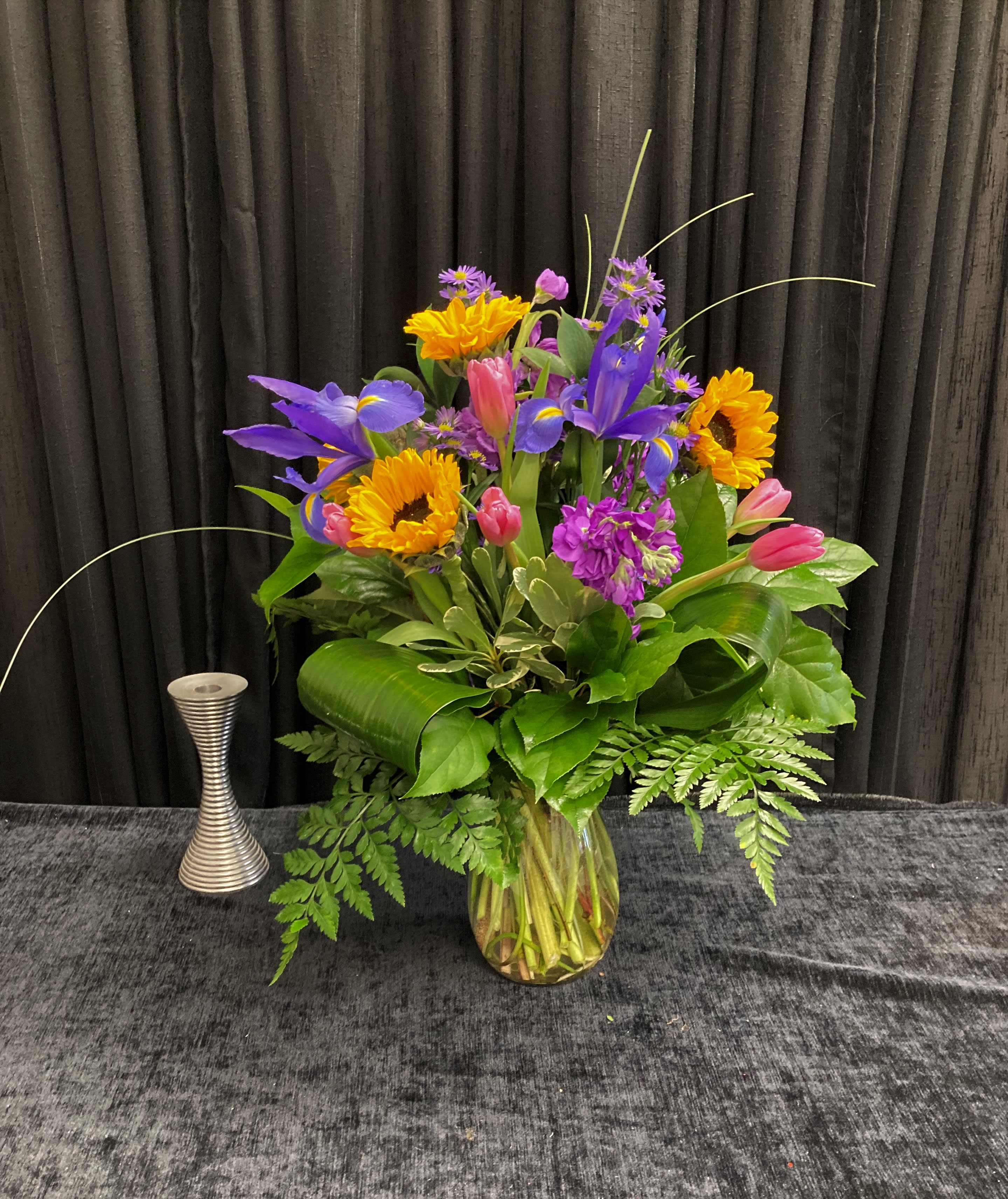 Colorful bouquet of sunflowers, irises, tulips, and purple flowers in a glass vase