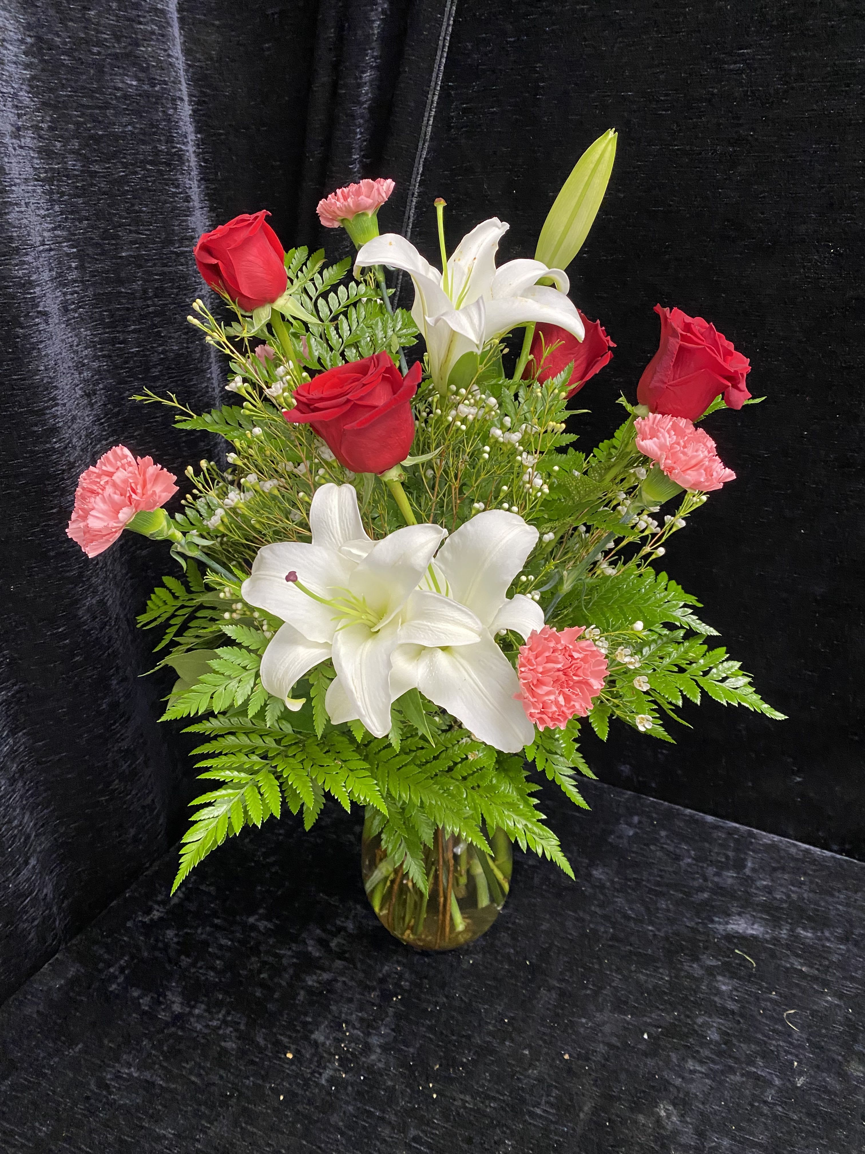 Bouquet of red roses, white lilies, and pink carnations in a glass vase